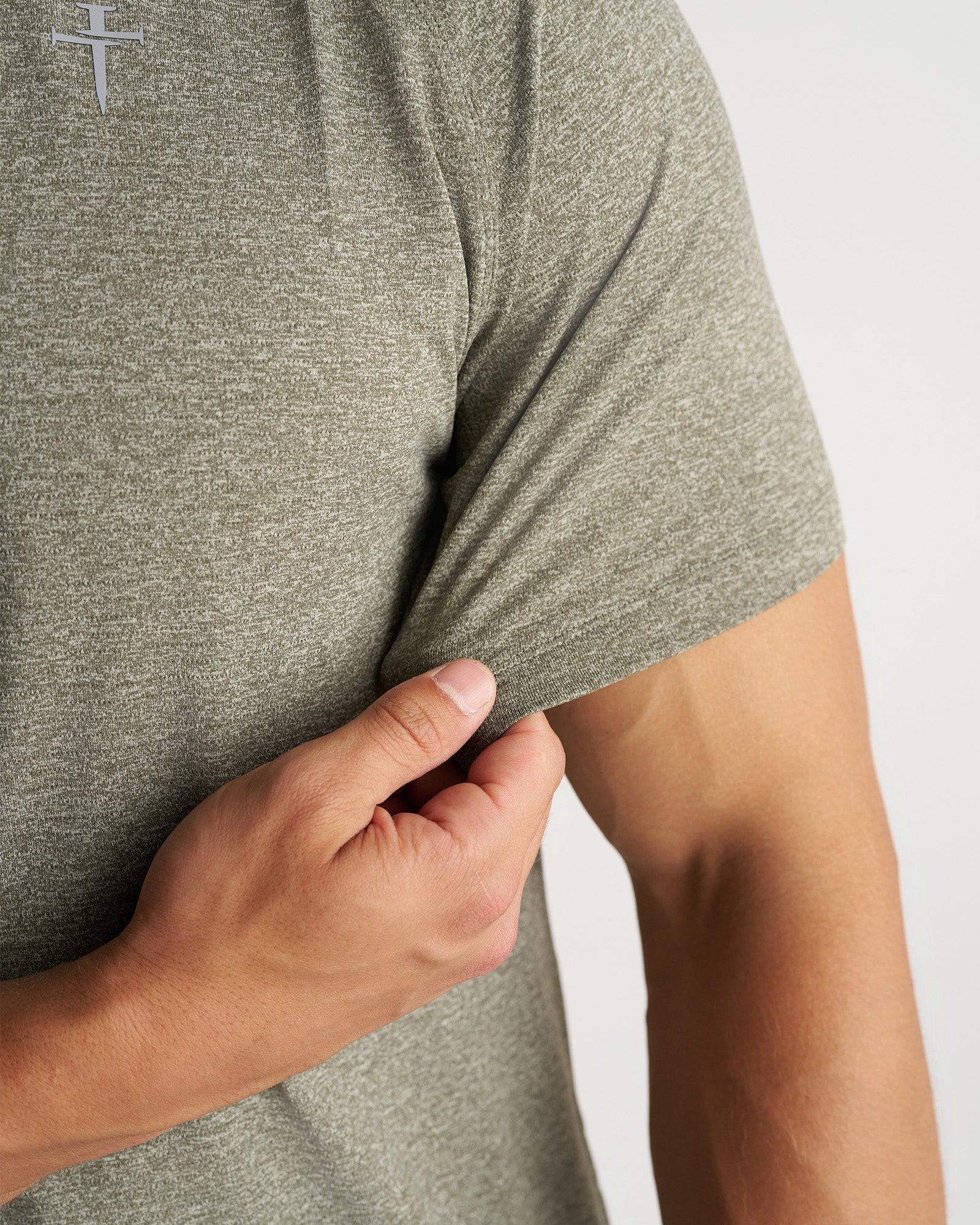 Close-up detail of the Aion-Lite Tee Cross in Sage Marl showing fabric stretch and sleeve hem being pulled.