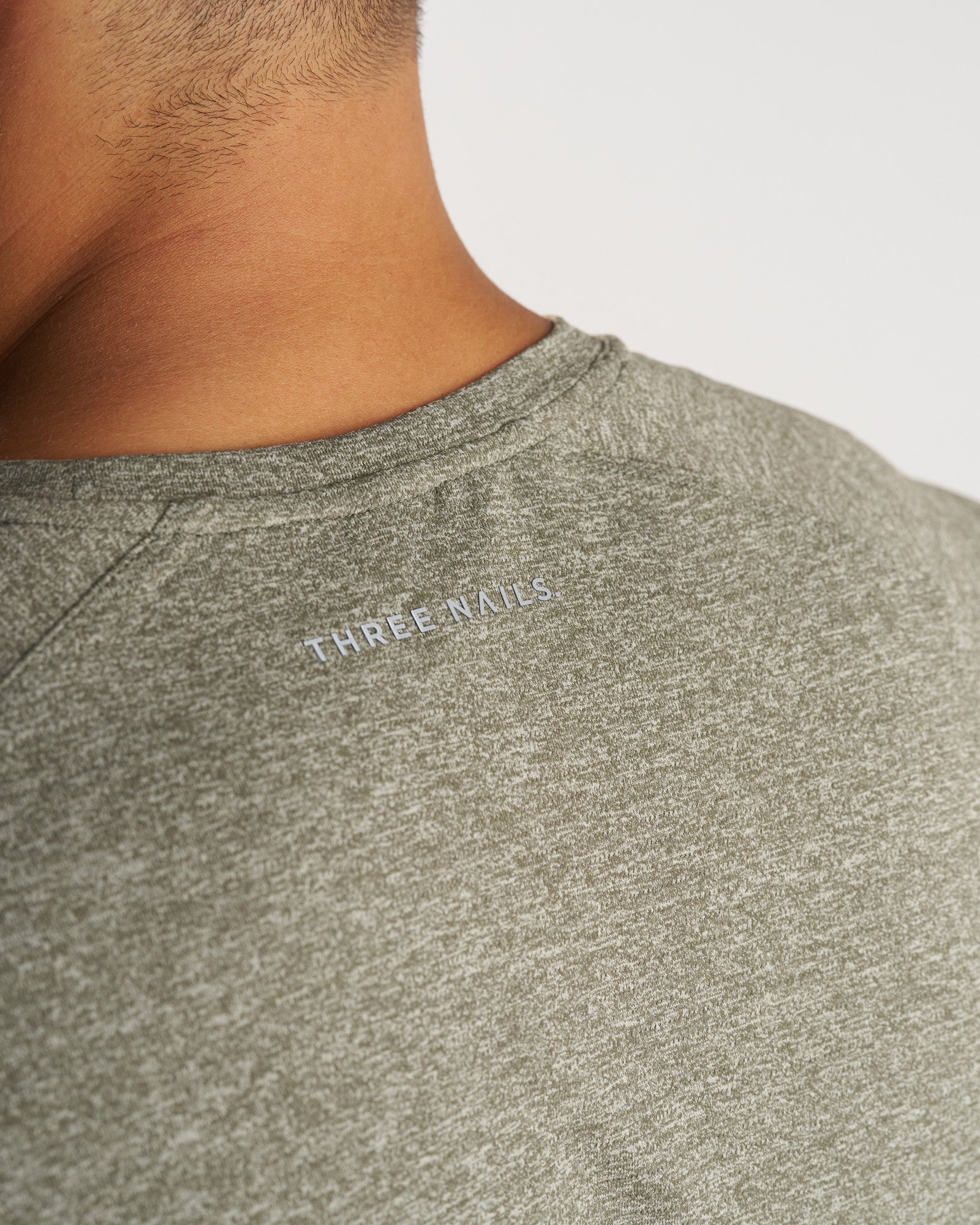 Close-up of the back neckline of the Aion-Lite Tee Cross in Sage Marl showing the Three Nails logo print.