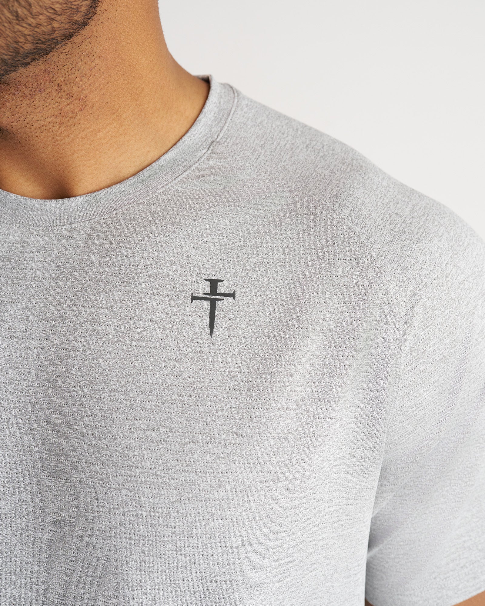 Close-up detail shot of the Aion-Lite Tee Cross in Grey Marl showing the nail cross logo on the chest.