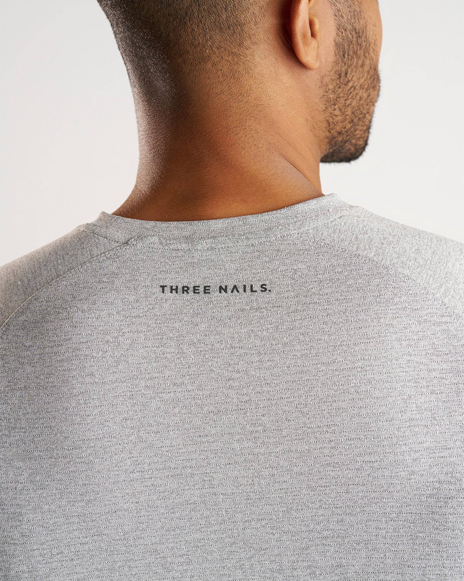 Close-up back neck detail of the Aion-Lite Tee Cross in Grey Marl showing the Three Nails. logo print.
