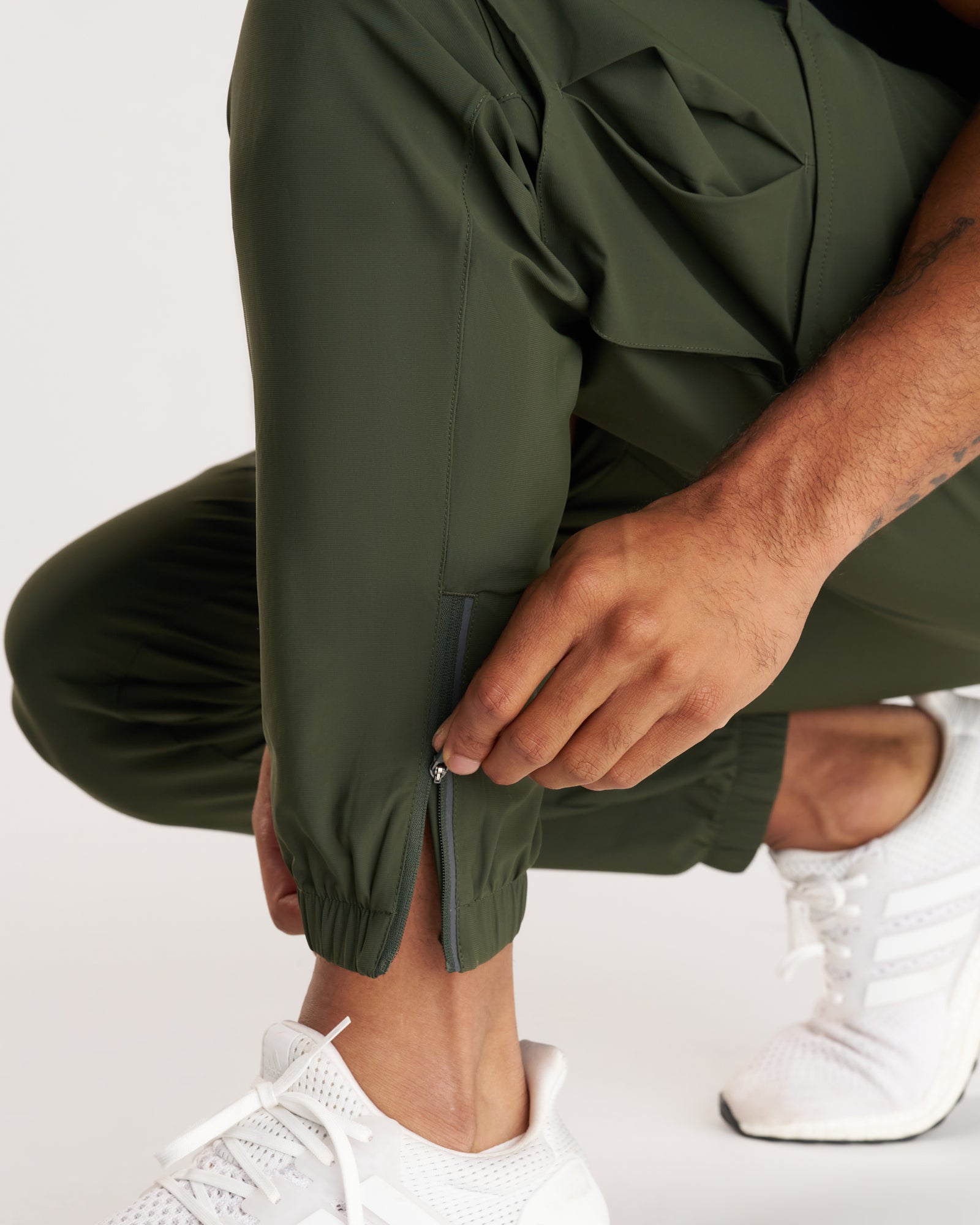 Close-up of Vapor-Lite Cargo Jogger in Dark Pine showing ankle zip detail on a crouching model.