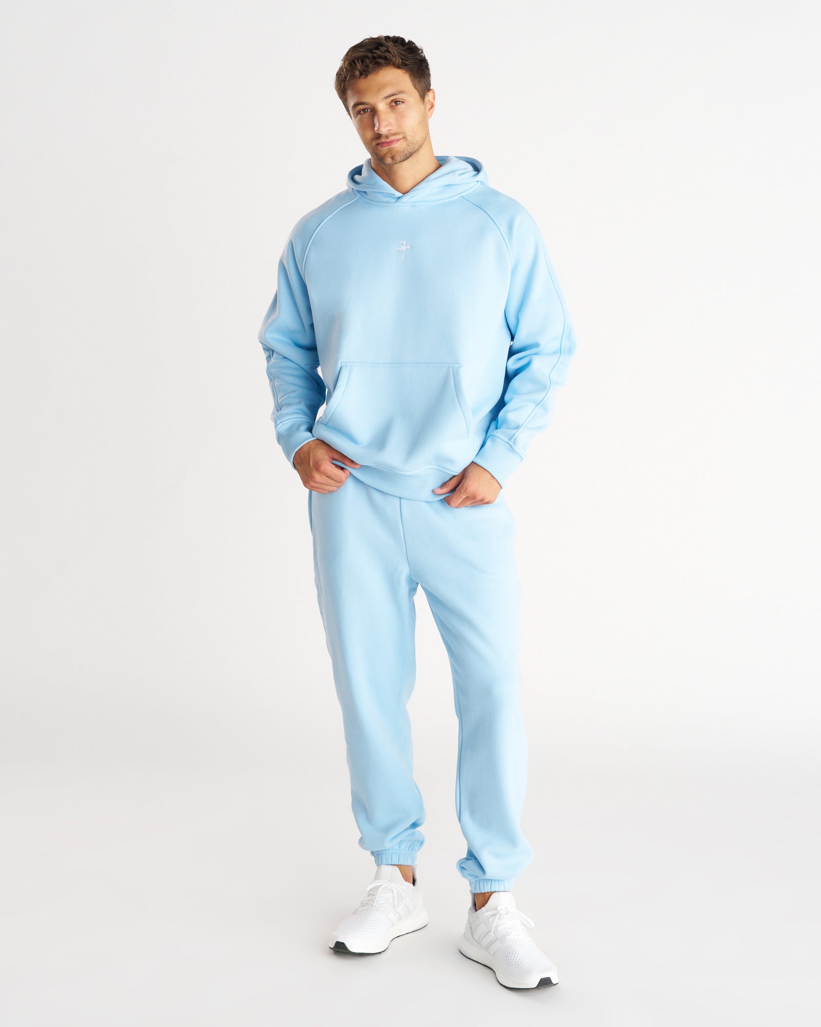 Man wearing Sky Blue Signature Fleece Sweatpants with matching hoodie, front view, white sneakers, plain background.