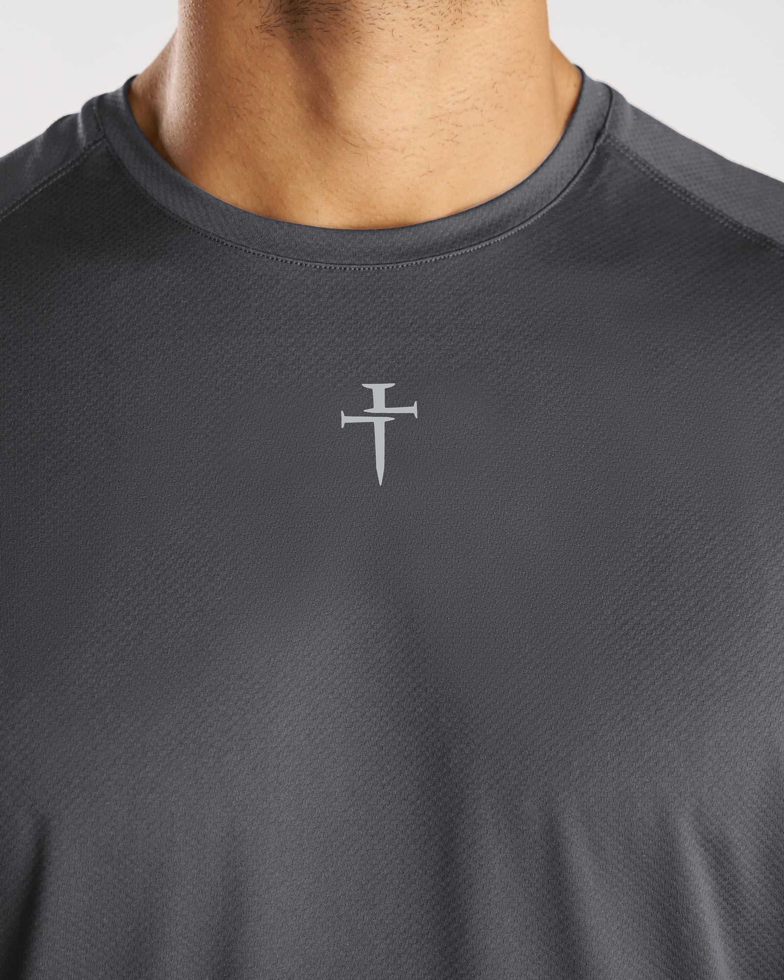 Close-up chest detail of the Pro-Tech Tee Cross in Space Grey showing a nail cross logo on grey athletic fabric.