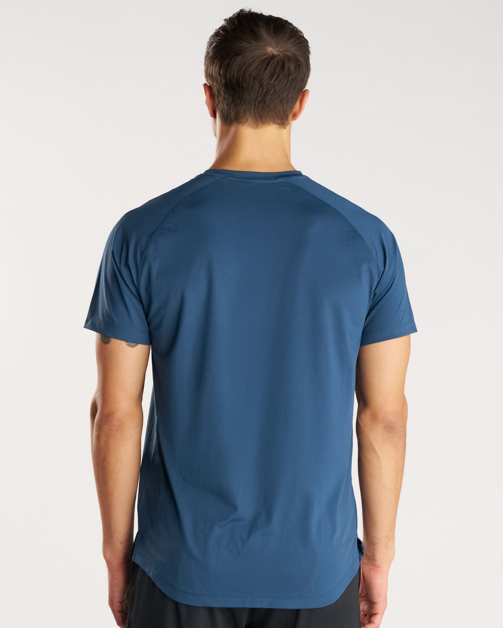 Back view of a male model wearing the Pro-Tech Tee Cross in Midnight Navy, a blue athletic tee with raglan sleeves.