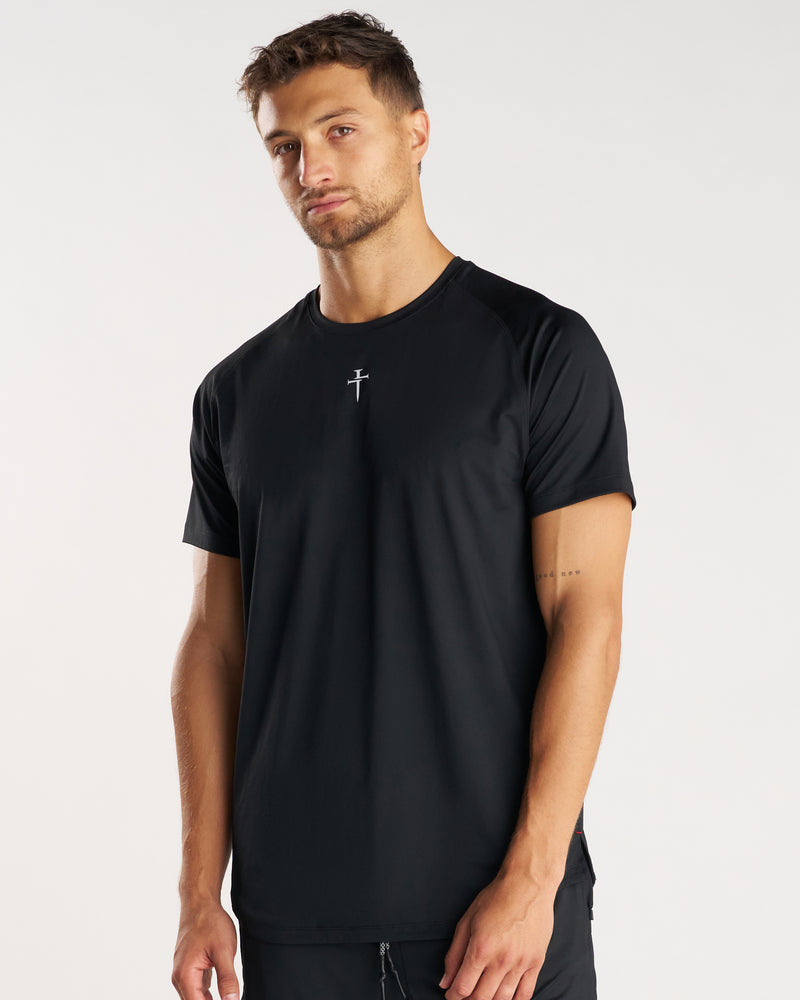 Man wearing black Pro-Tech Tee Cross at a slight angle, small cross logo centered on chest.