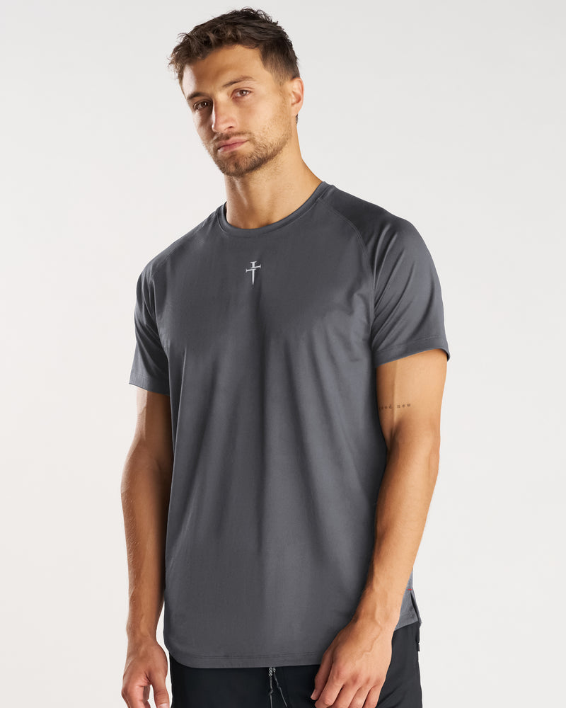 Male model wearing charcoal Pro-Tech Tee with small cross logo, shown from slight side angle.