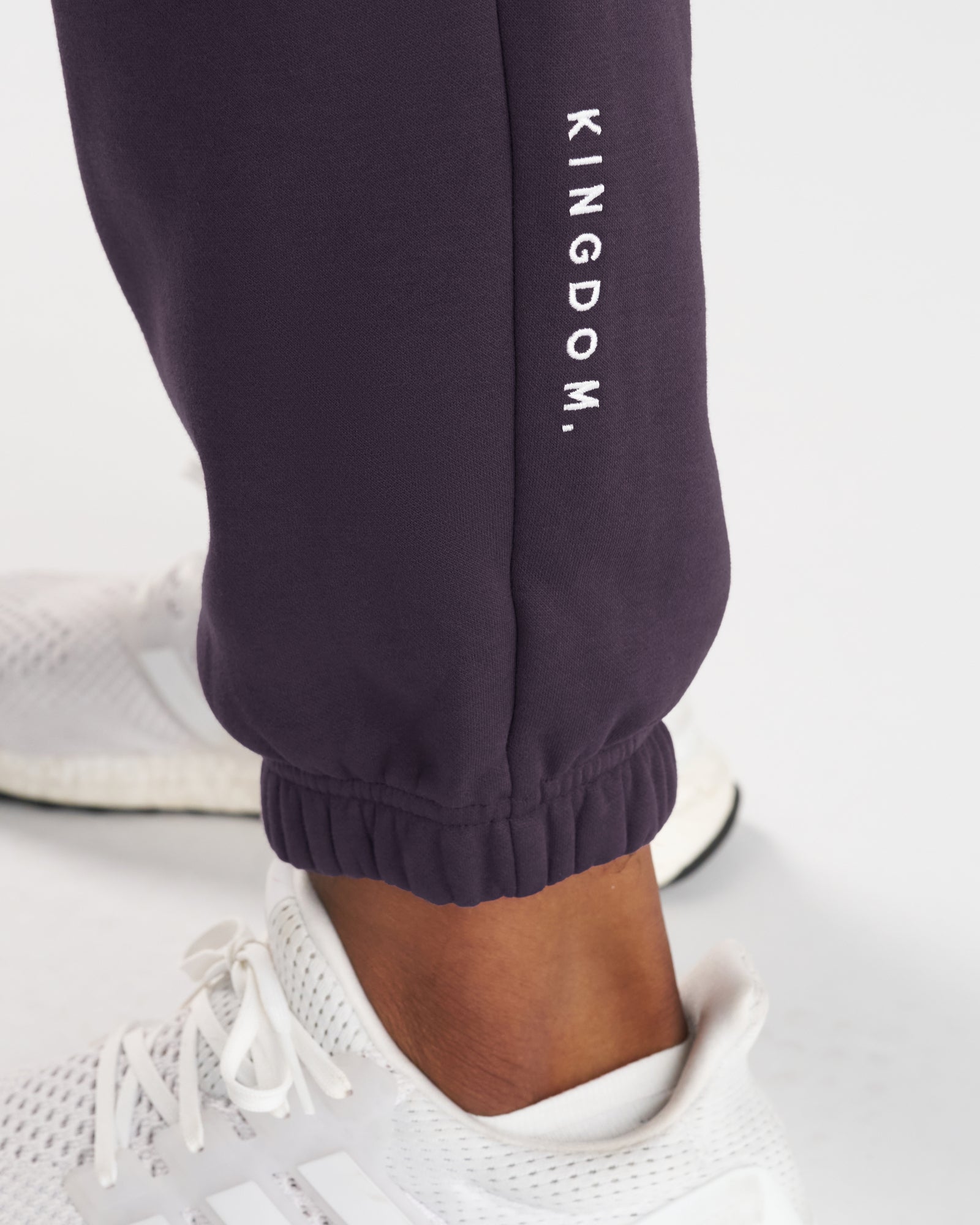 Close-up of Signature Fleece Sweatpants in Nightshade showing the ribbed ankle cuff and embroidered KINGDOM. text on the leg.