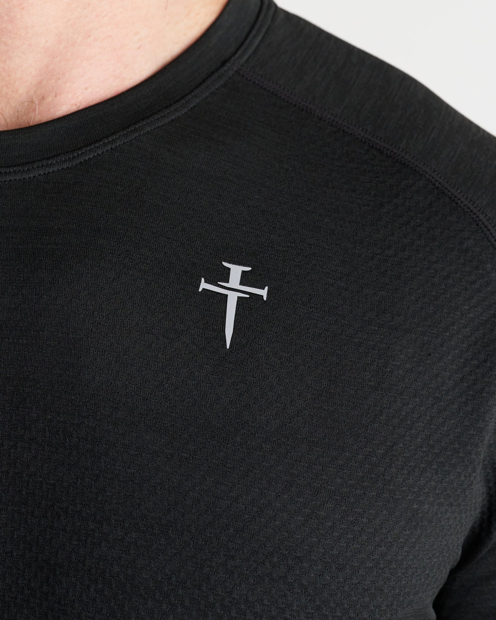 Close-up of Three Nails cross logo on chest of Black Marl Seamless Tee