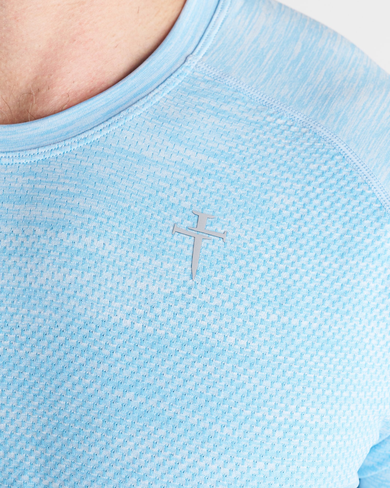 Close-up detail of the Sky Blue Seamless Tee showing mesh fabric texture and silver Three Nails logo on chest.