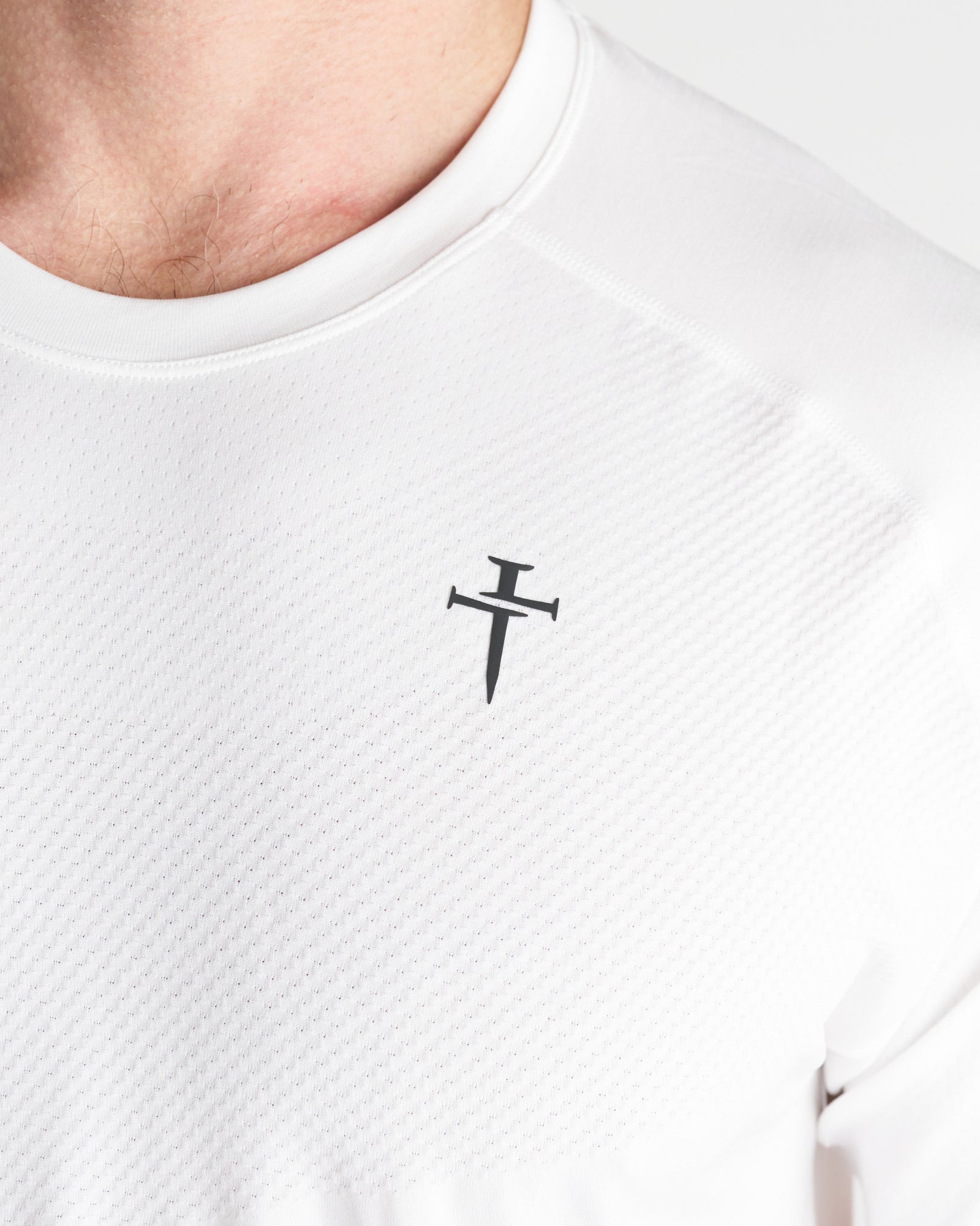 Close-up of the white Seamless Tee chest area showing the Three Nails cross logo on mesh fabric.