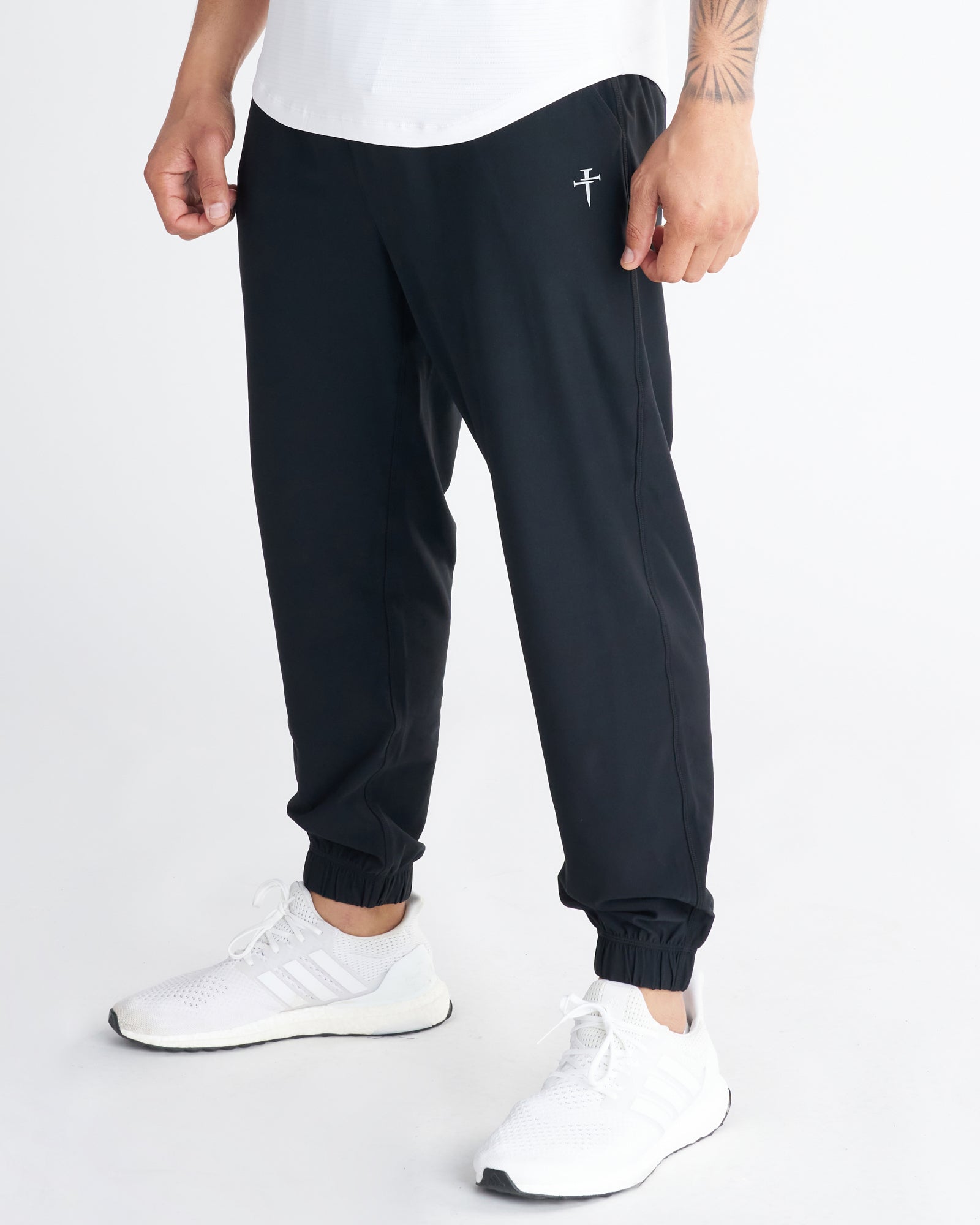 Haven Performance Jogger in black on a male model, front side angle, with ribbed cuffs and a small cross logo near the waistband.