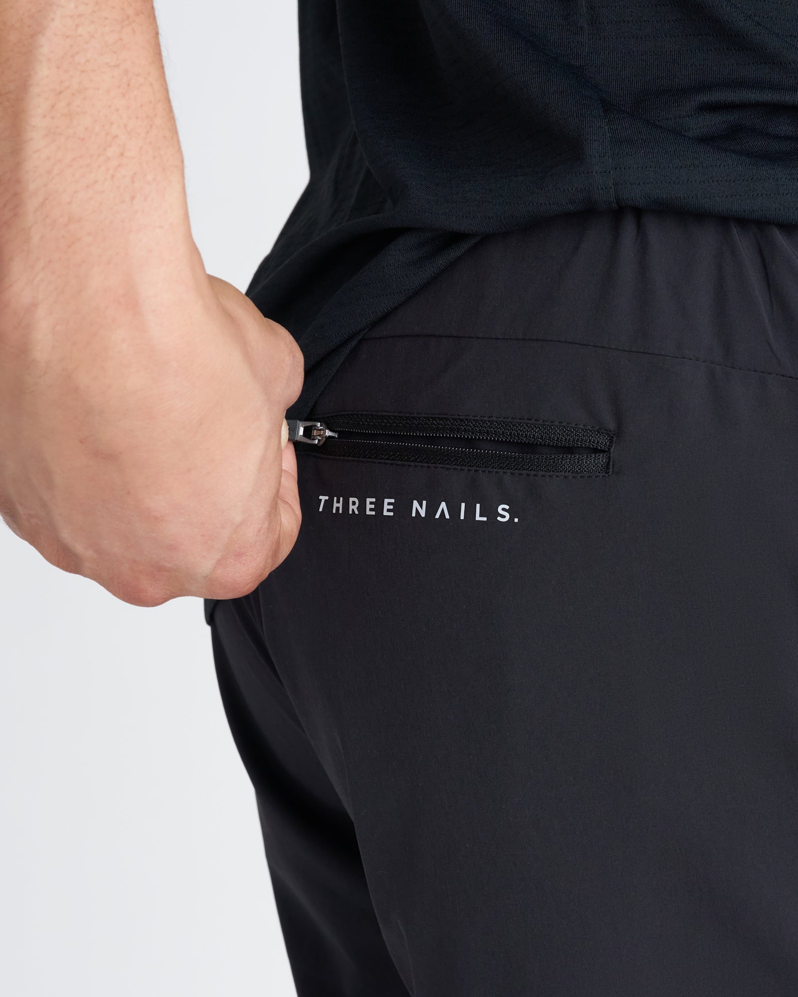 Close-up of Pulse Tech Linerless Short in black showing zippered back pocket with Three Nails branding.
