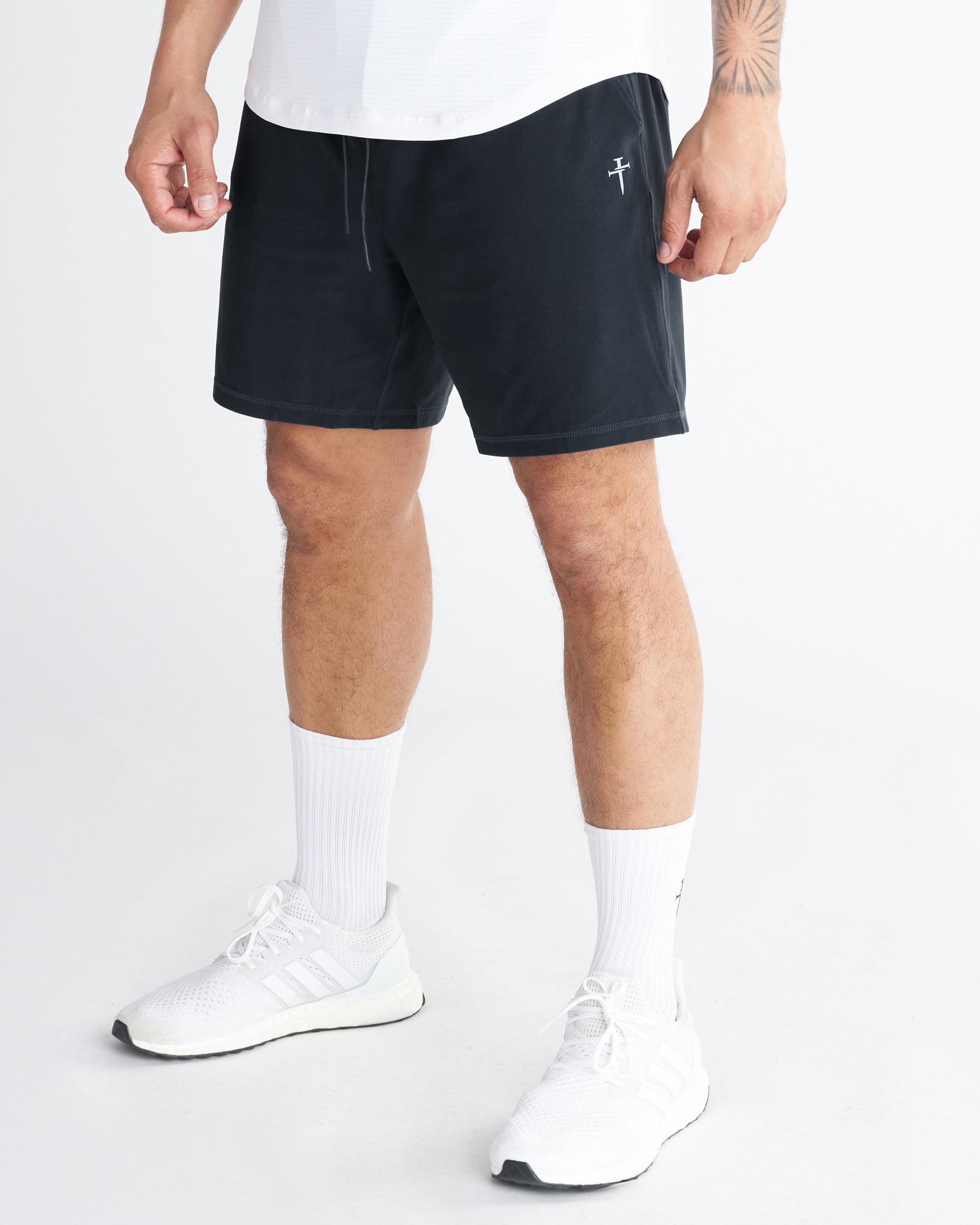Haven Performance Short in black on a male model, front side angle view, paired with white Adidas sneakers.