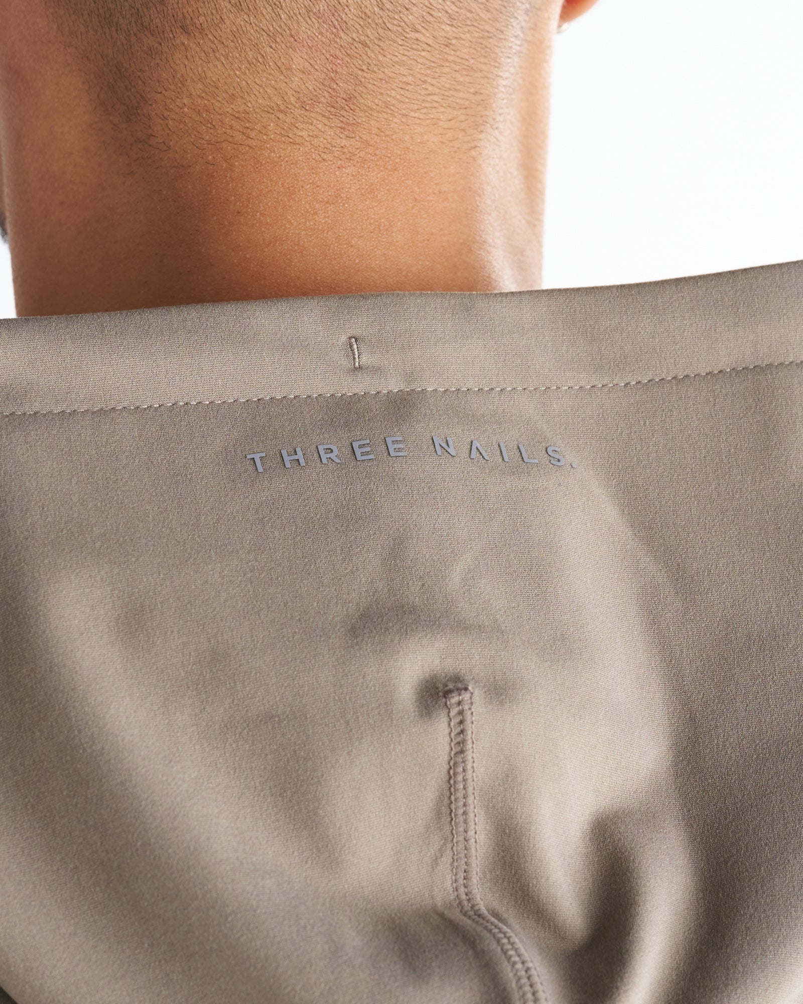 Close-up of the Haven Performance Hoodie in Sand showing the embossed Three Nails logo on the back collar area.