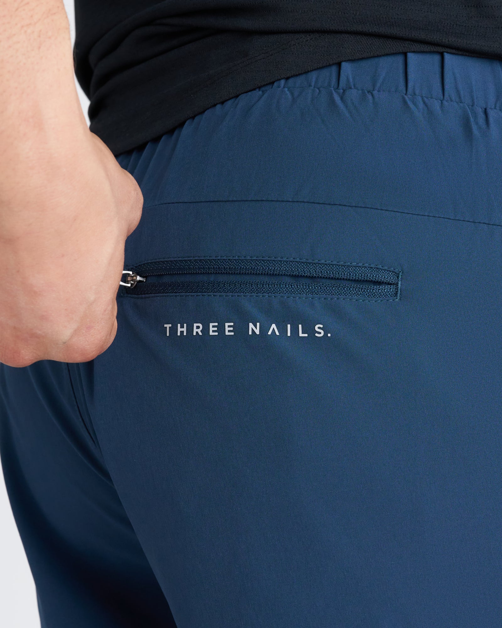 Close-up of Pulse Tech Linerless Short in Midnight Navy showing zippered back pocket with Three Nails branding.