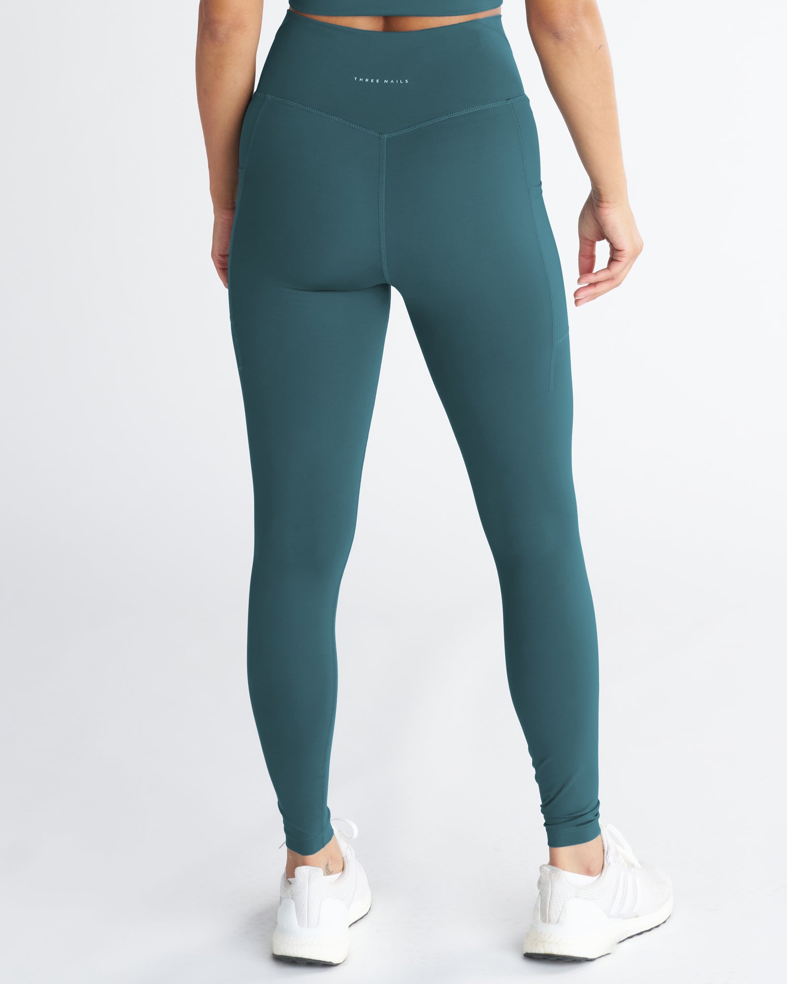 Back view of the Endura-Train Pocket Legging in Teal, showing V-waistband and side pockets, paired with white sneakers.