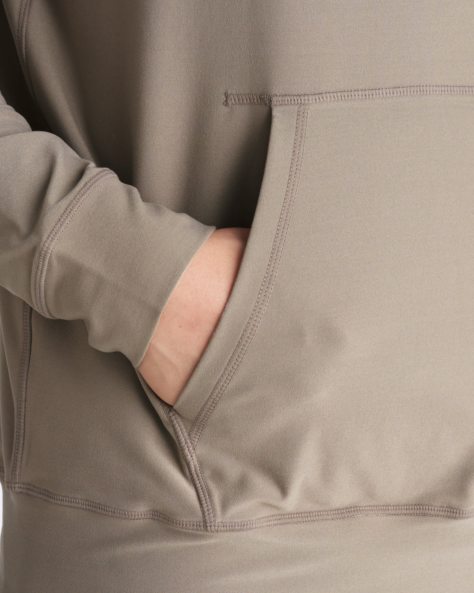 Haven Performance Hoodie in Sand, close-up detail of kangaroo pocket with hand inserted showing stitching and fabric texture.