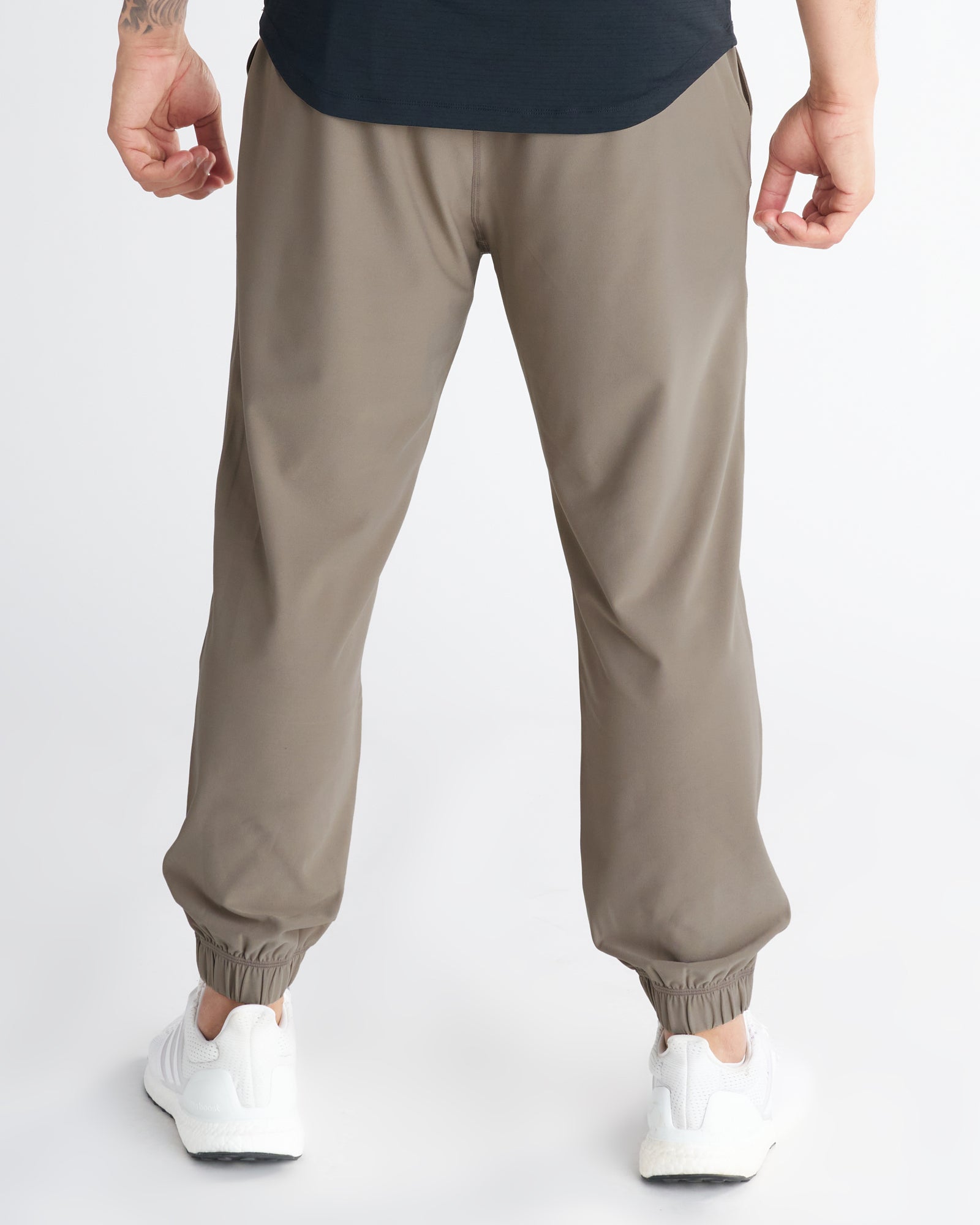 Back view of Haven Performance Jogger in Sand with elastic cuffs, paired with white sneakers.