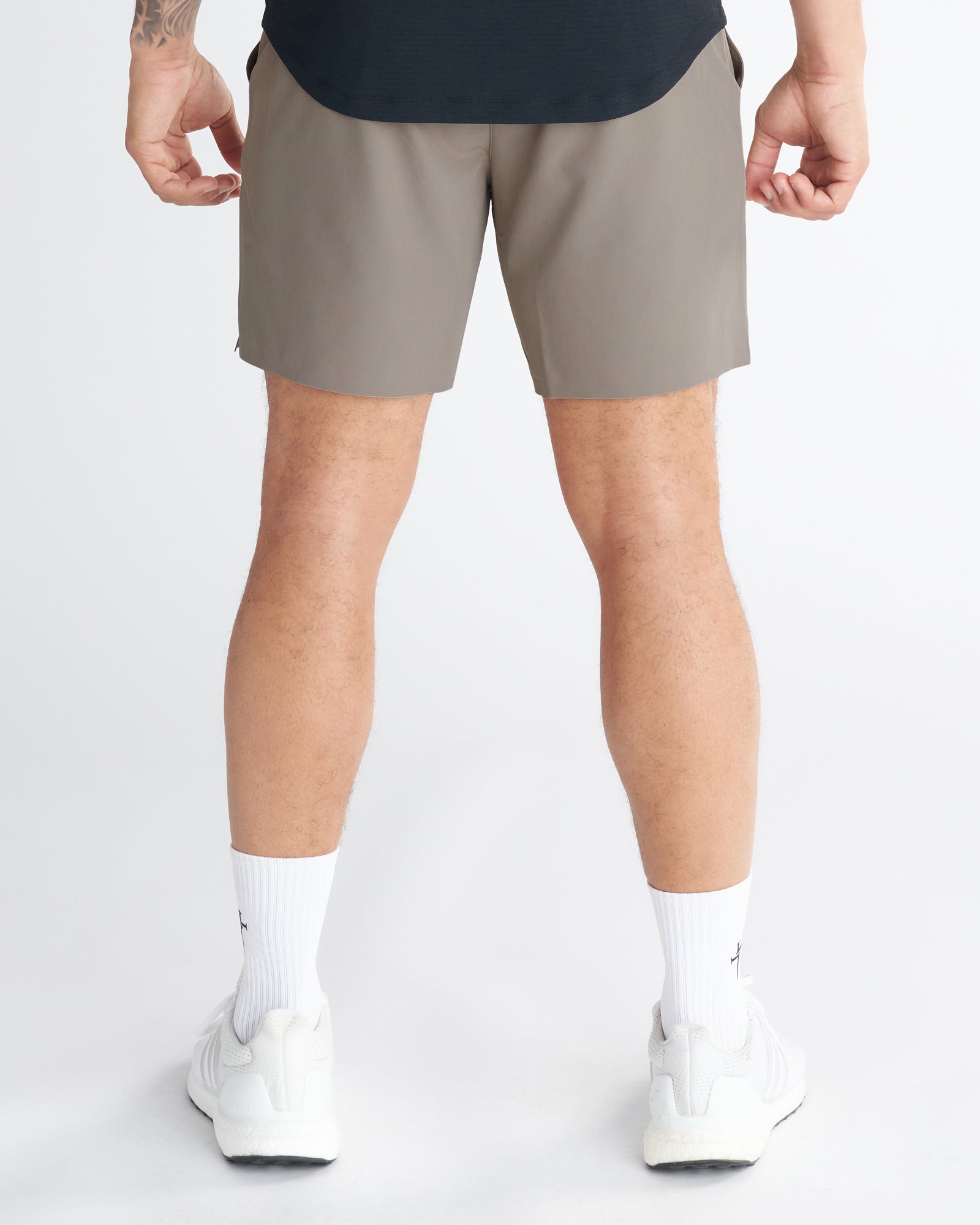 Back view of model wearing Pulse Tech Linerless Short in Sand with white sneakers and socks.