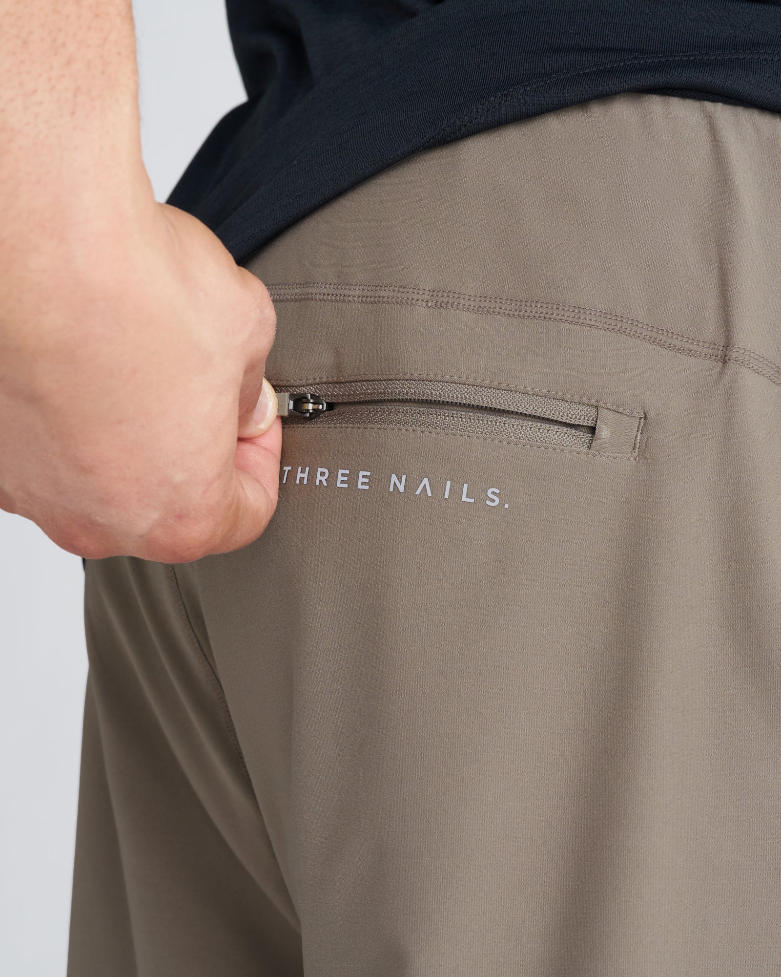 Close-up of Haven Performance Jogger in Sand showing zippered back pocket with Three Nails branding.