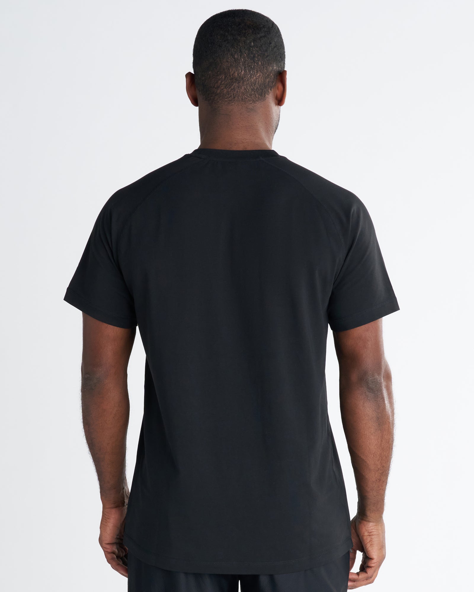 Back view of a man wearing the Core Tee in black, showing a clean plain back and raglan-style sleeves.