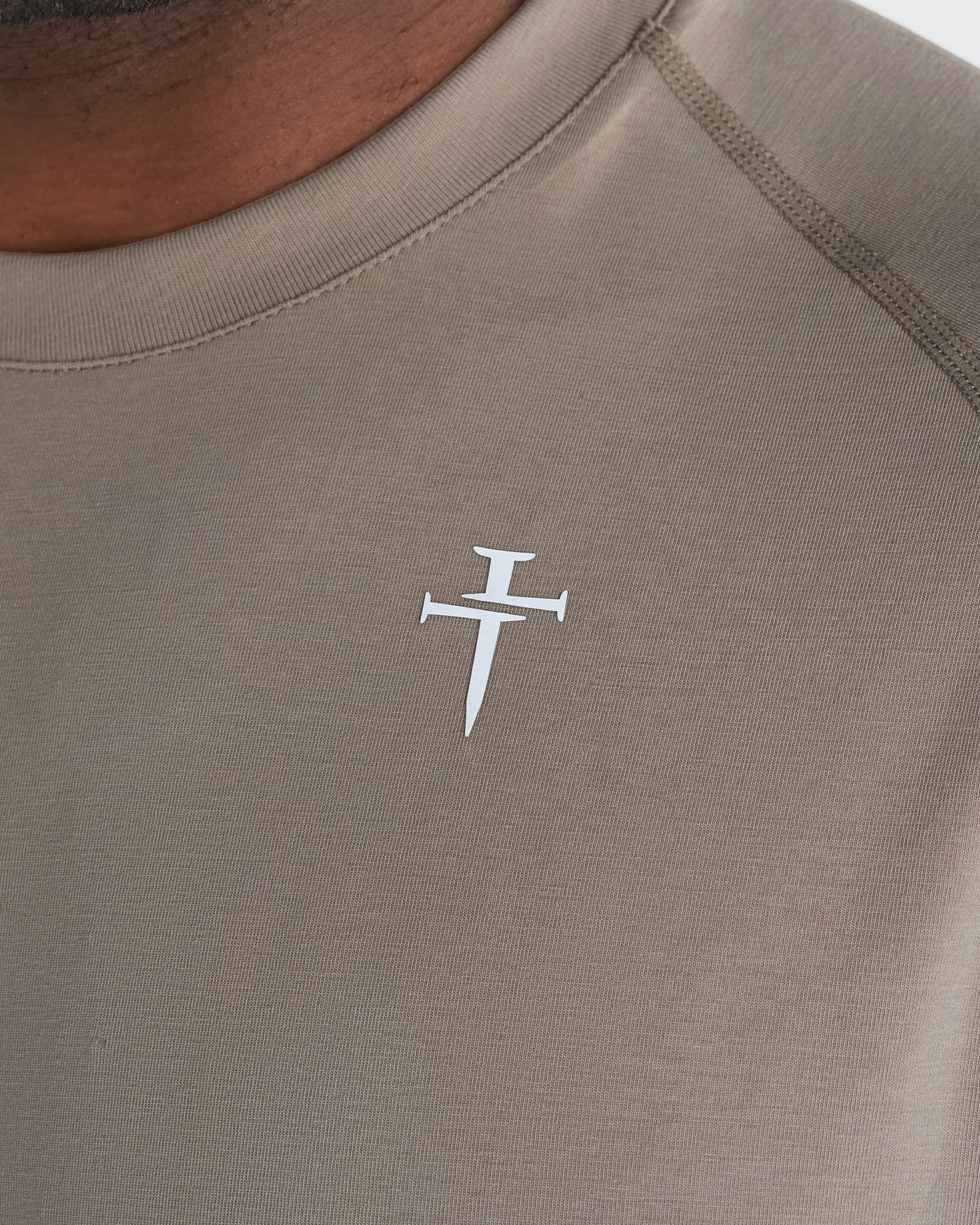 Close-up detail of the Core Tee in Sand showing the white Three Nails cross logo on the chest.