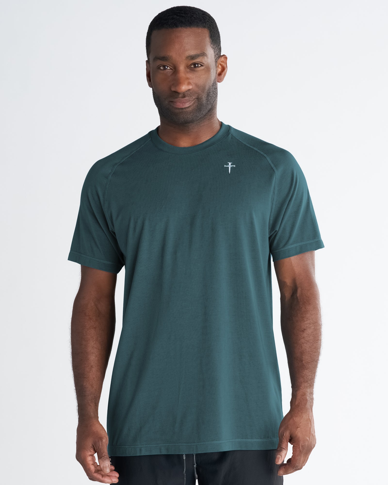 Man wearing Core Tee in teal, front view, with small cross logo on chest, raglan sleeves.