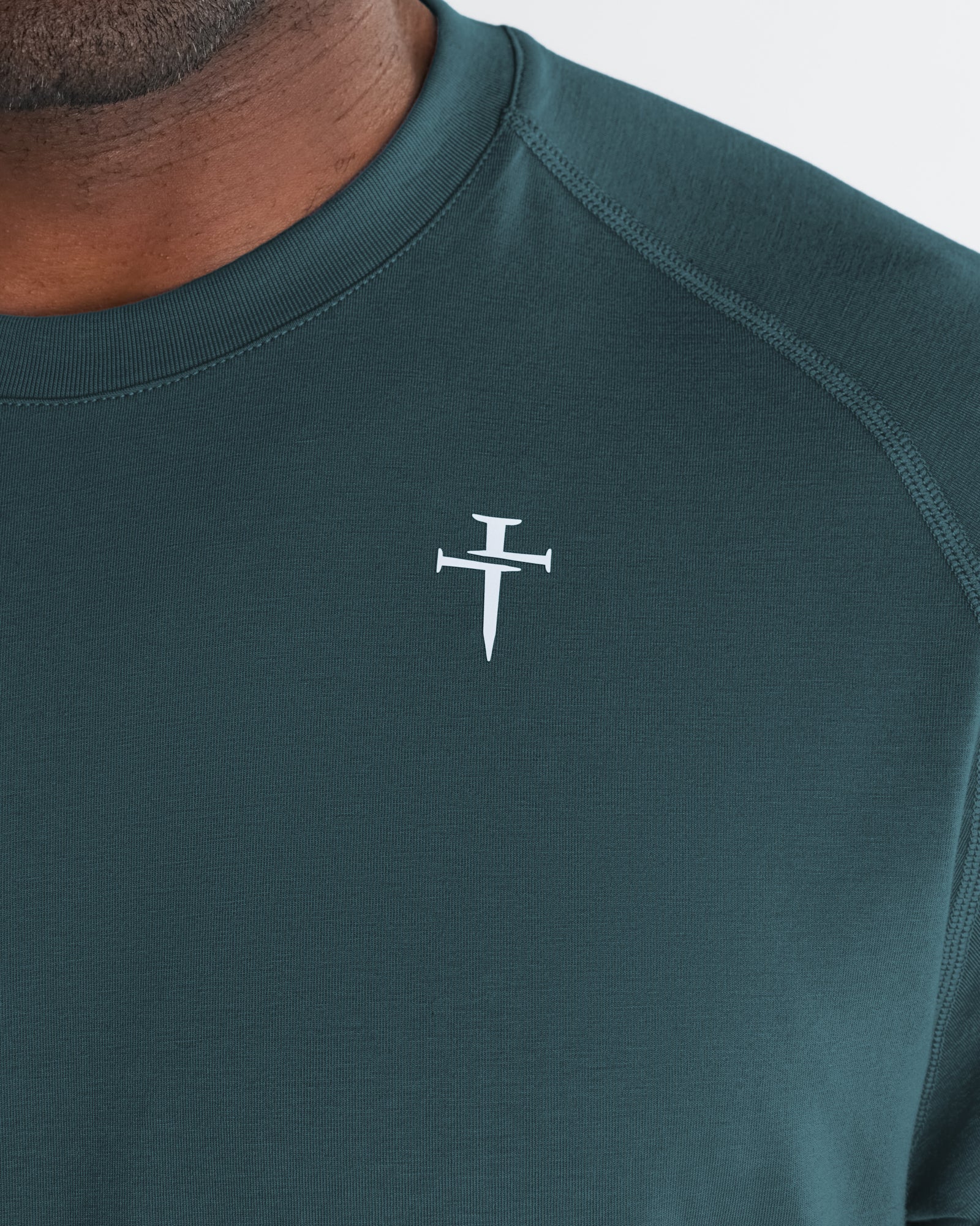 Close-up of Core Tee in Teal showing the three nails cross logo on the chest.