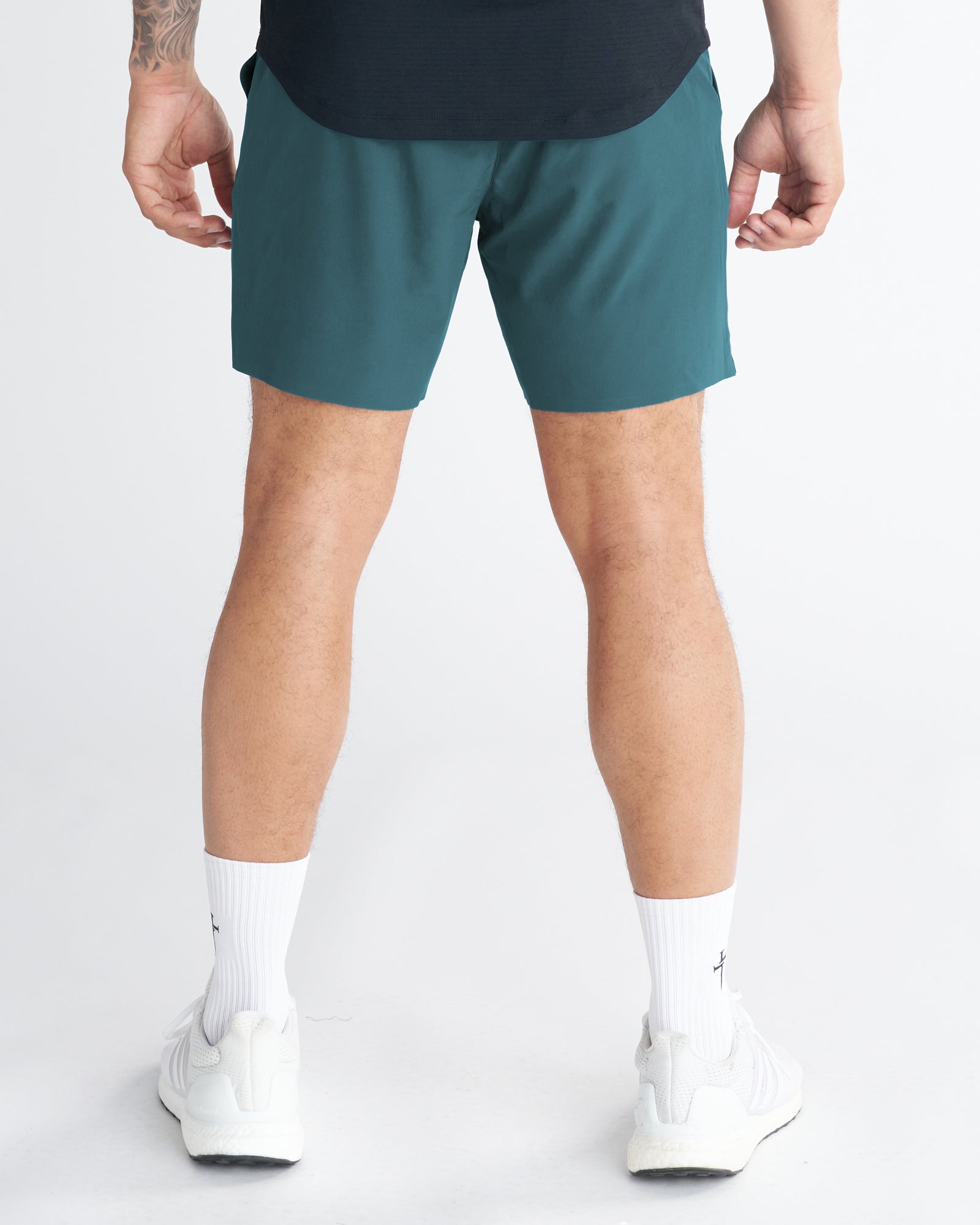 Back view of the Pulse Tech Linerless Short in Teal, shown on a standing model with white sneakers.
