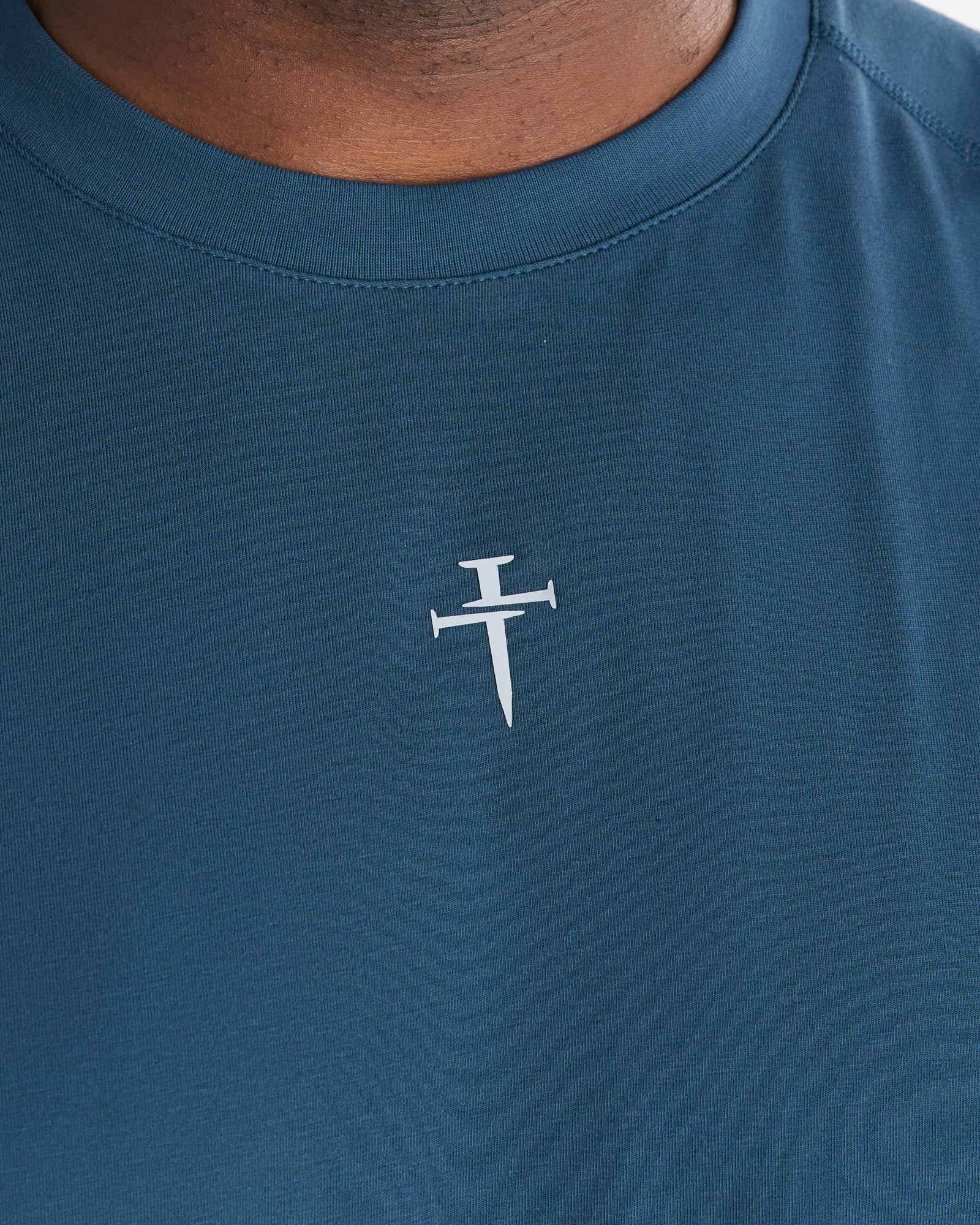 Close-up of the Core Raglan Cutoff Midnight Navy chest logo, a cross made of two nails.