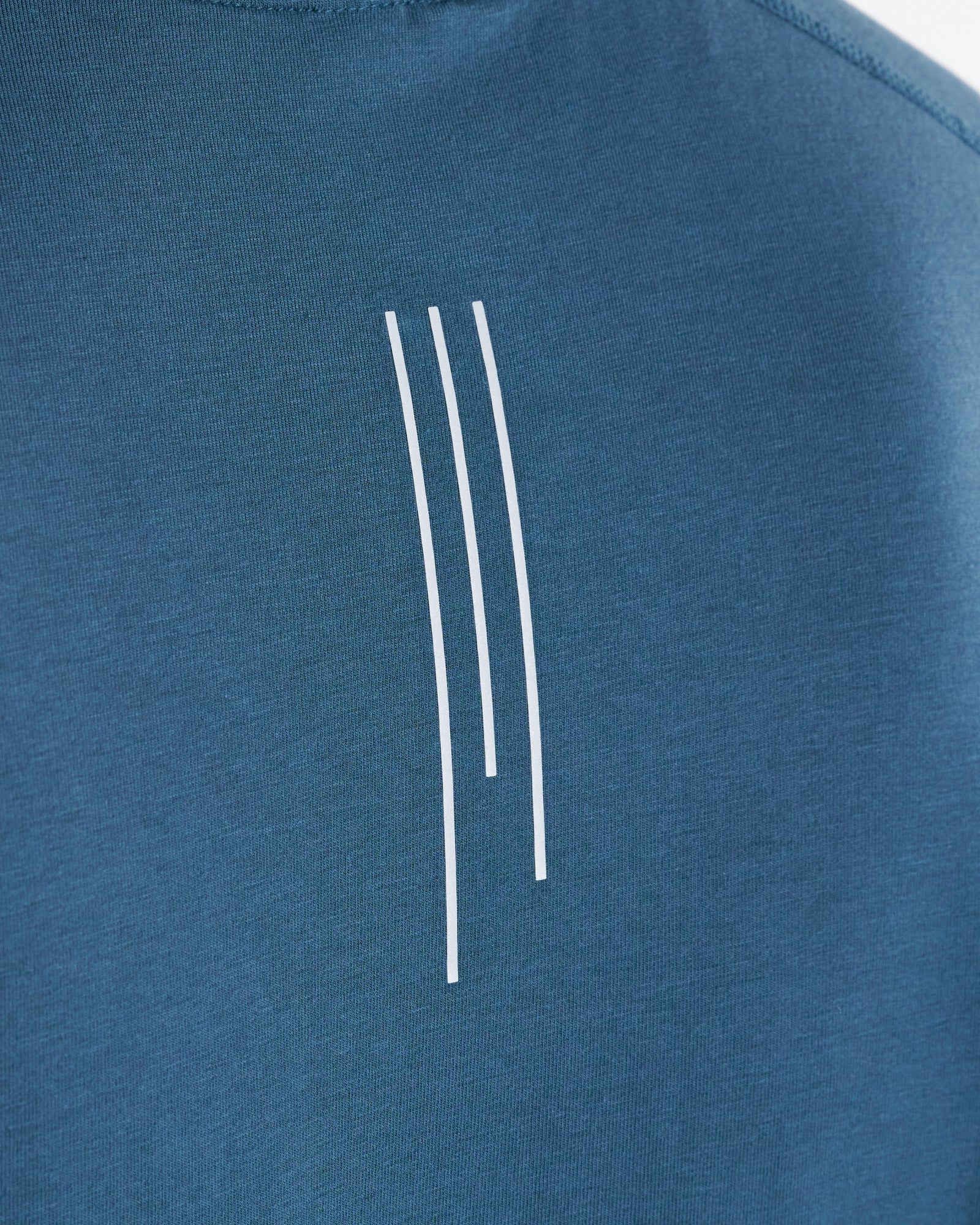 Close-up of the back graphic detail on the Core Raglan Cutoff in Midnight Navy, showing three white vertical lines.