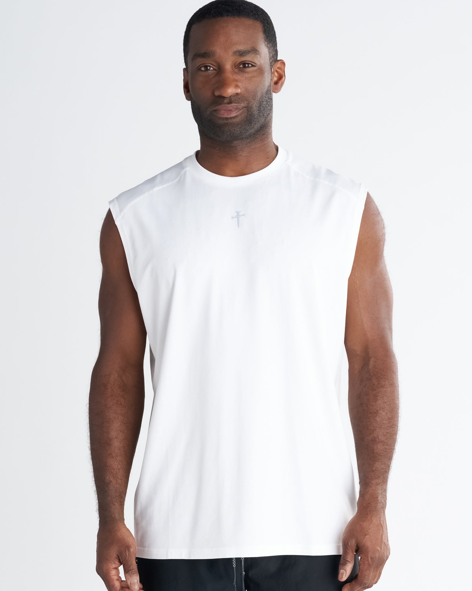 Man wearing white Core Raglan Cutoff tank top, front view, small cross graphic on chest.