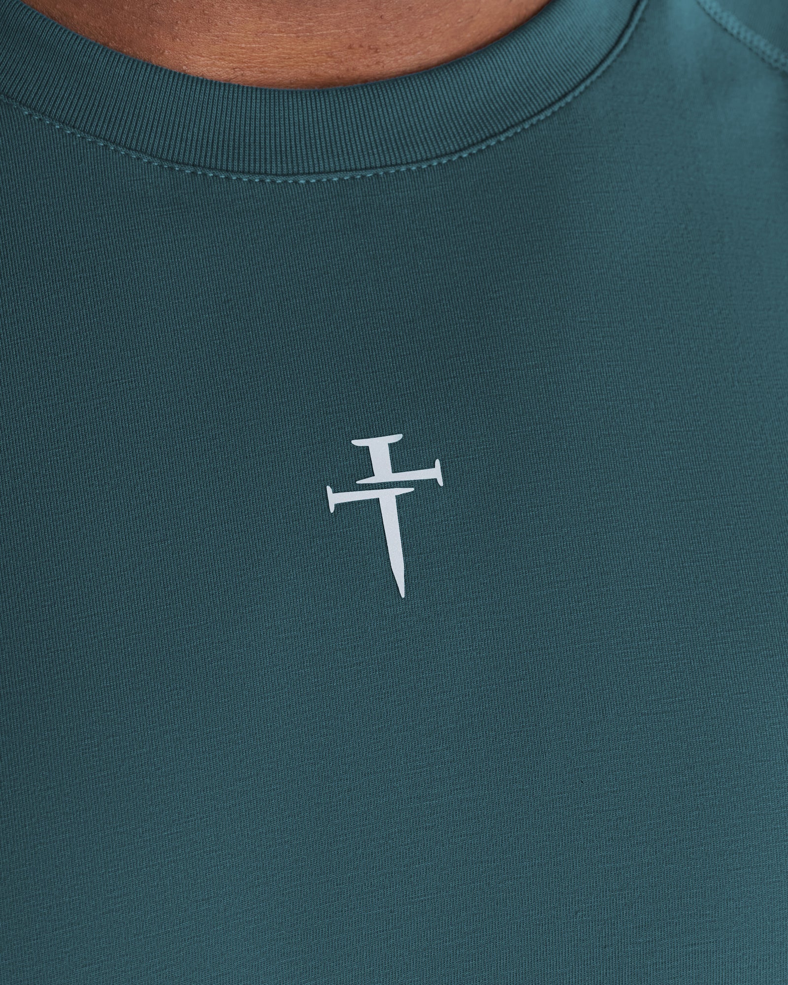 Close-up of the Three Nails logo on the chest of the Core Raglan Cutoff in teal.