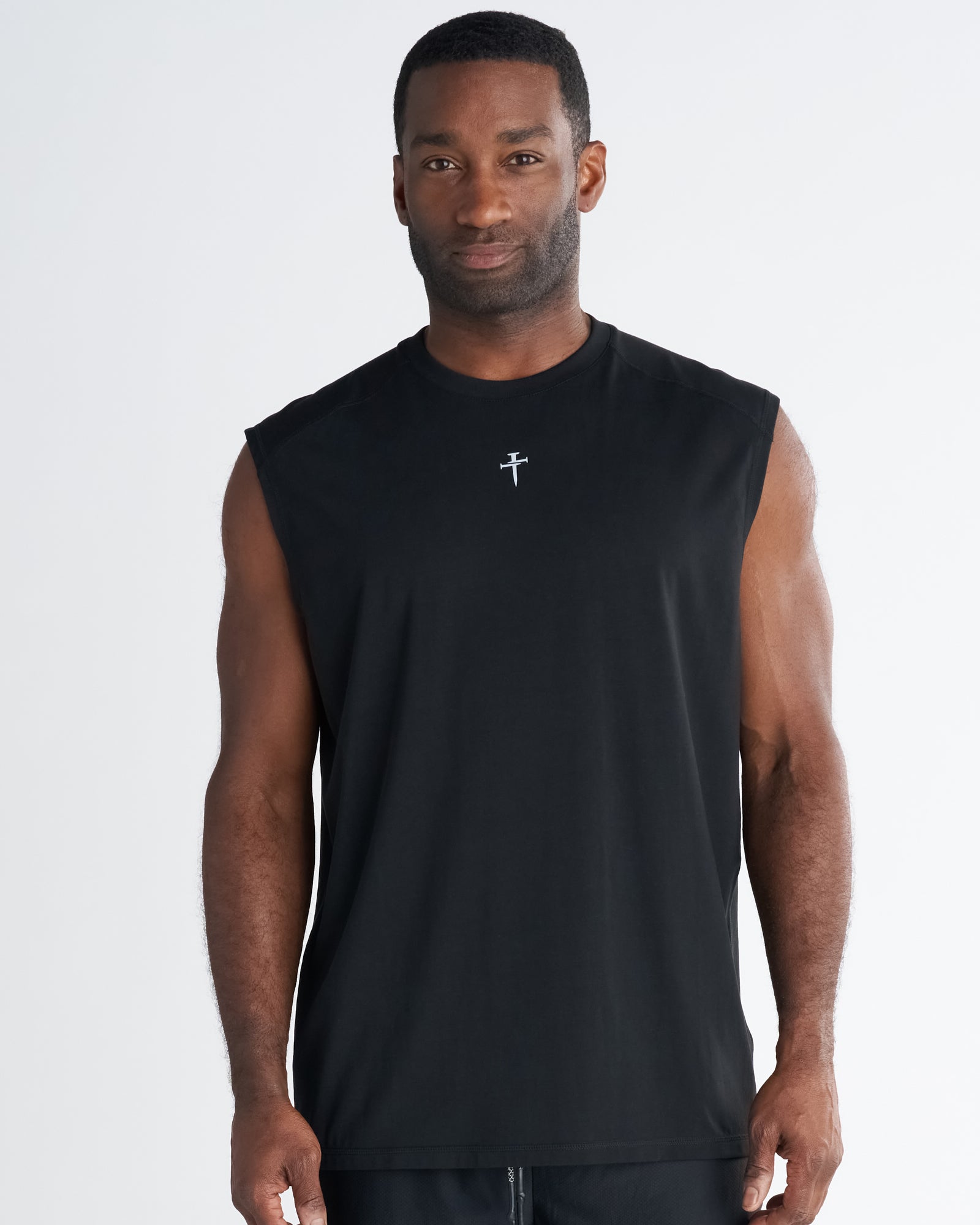 Man wearing black Core Raglan Cutoff tank, front view, with small cross logo at chest.