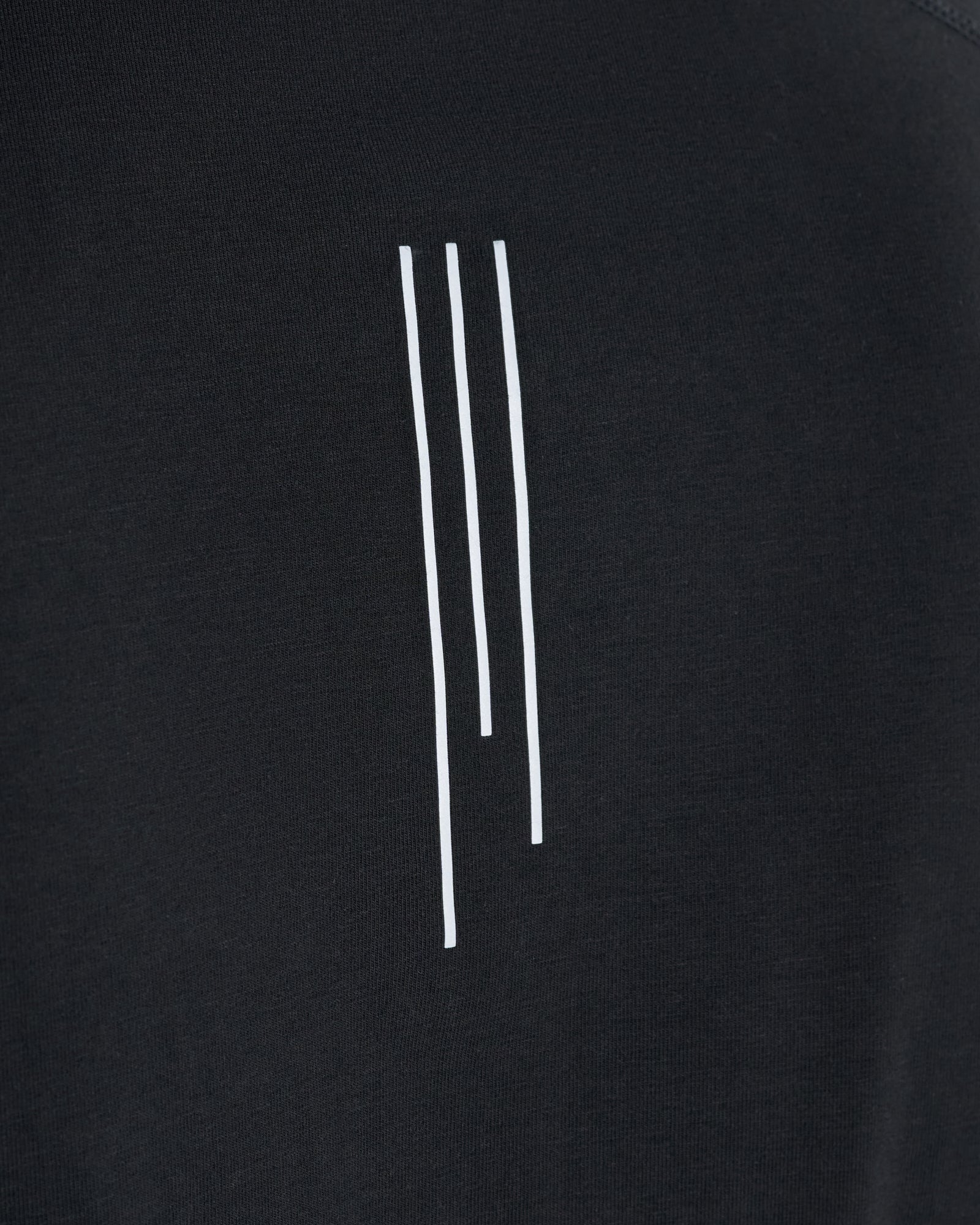 Close-up of the black Core Raglan Cutoff showing three vertical white lines printed on the chest fabric.