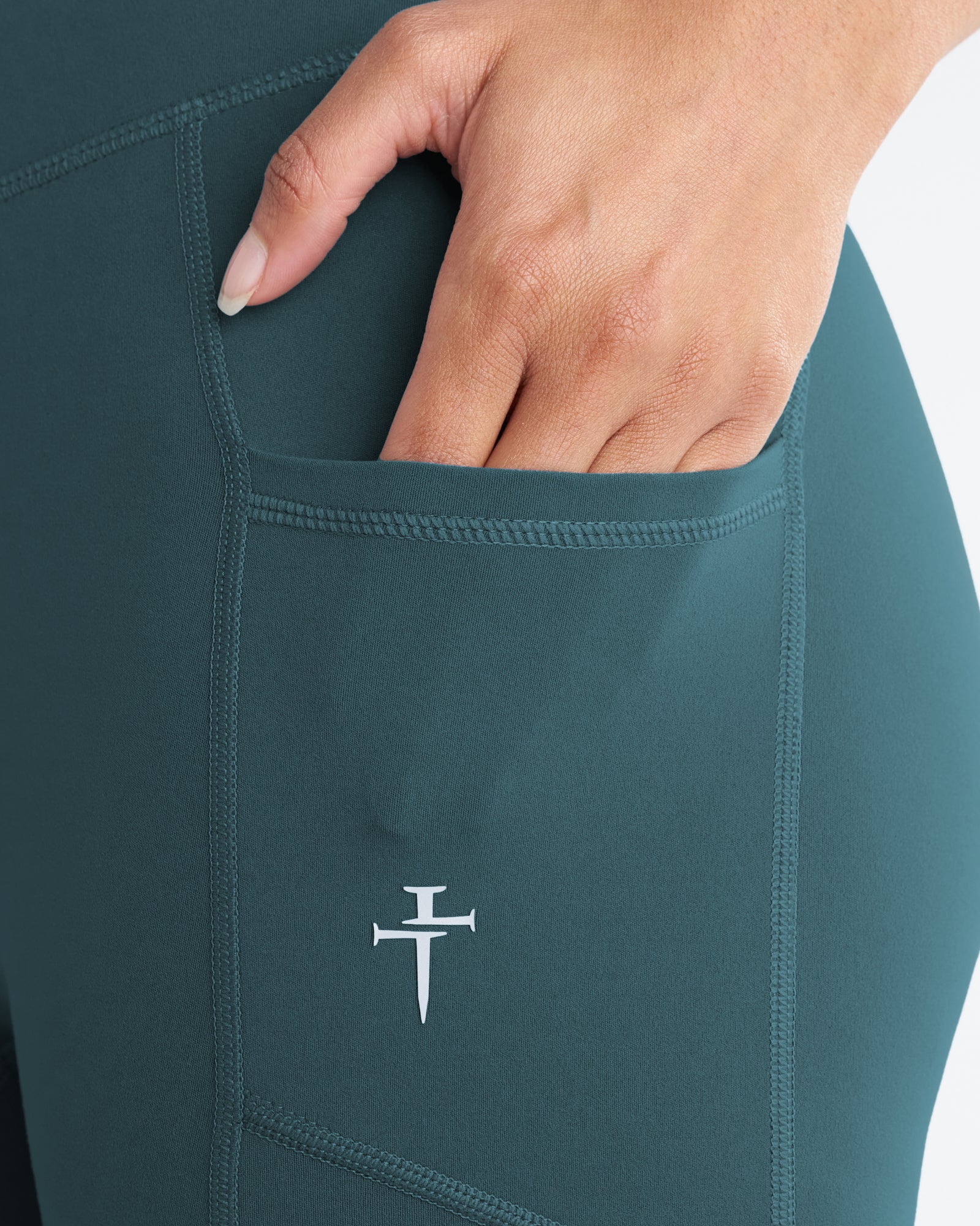 Close-up detail of the Nova Pocket Legging 27" in Teal showing a hand sliding into the side pocket.