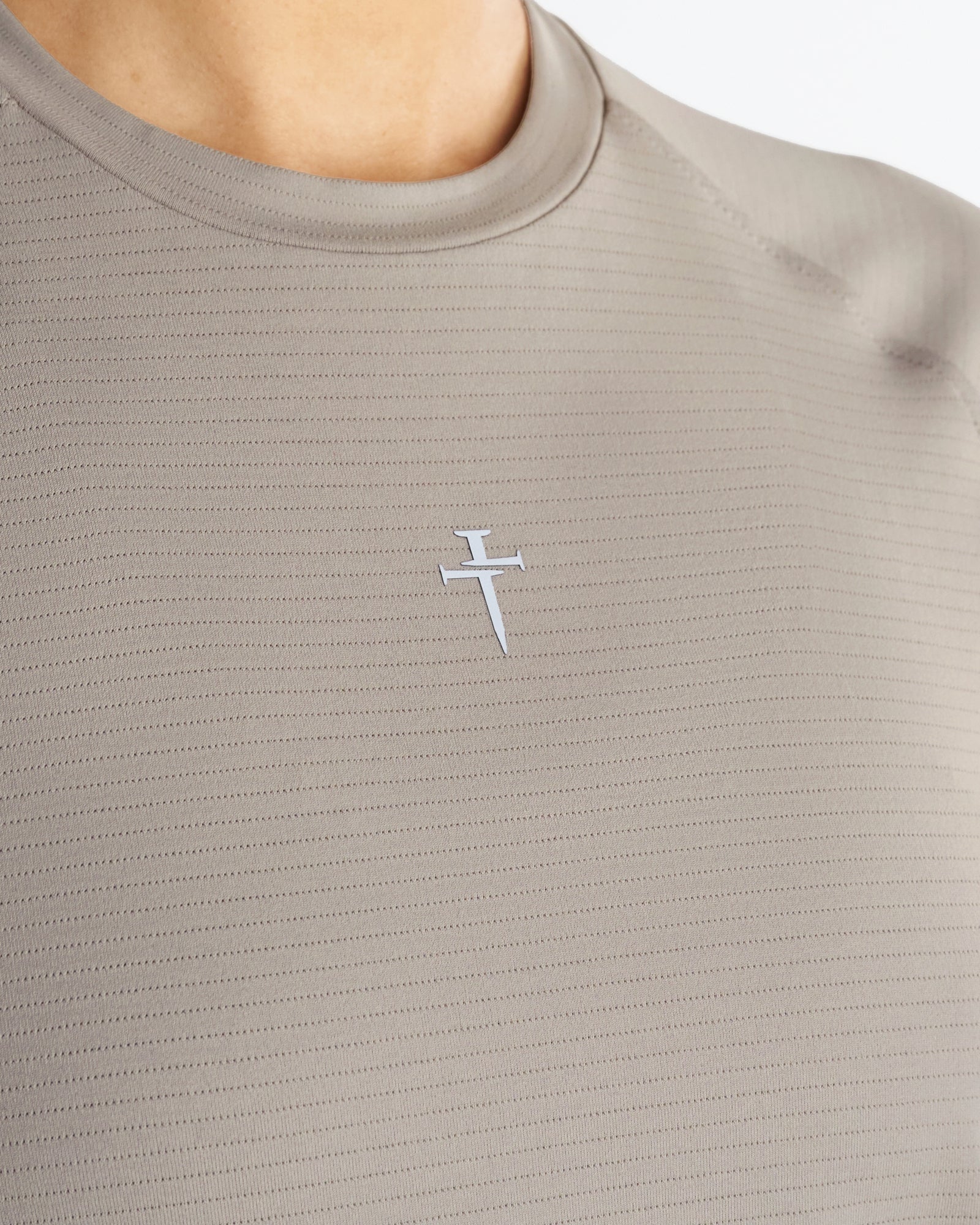 Close-up of the sand Women's Aion-Lite Tee Cross showing a small white cross logo on ribbed fabric.