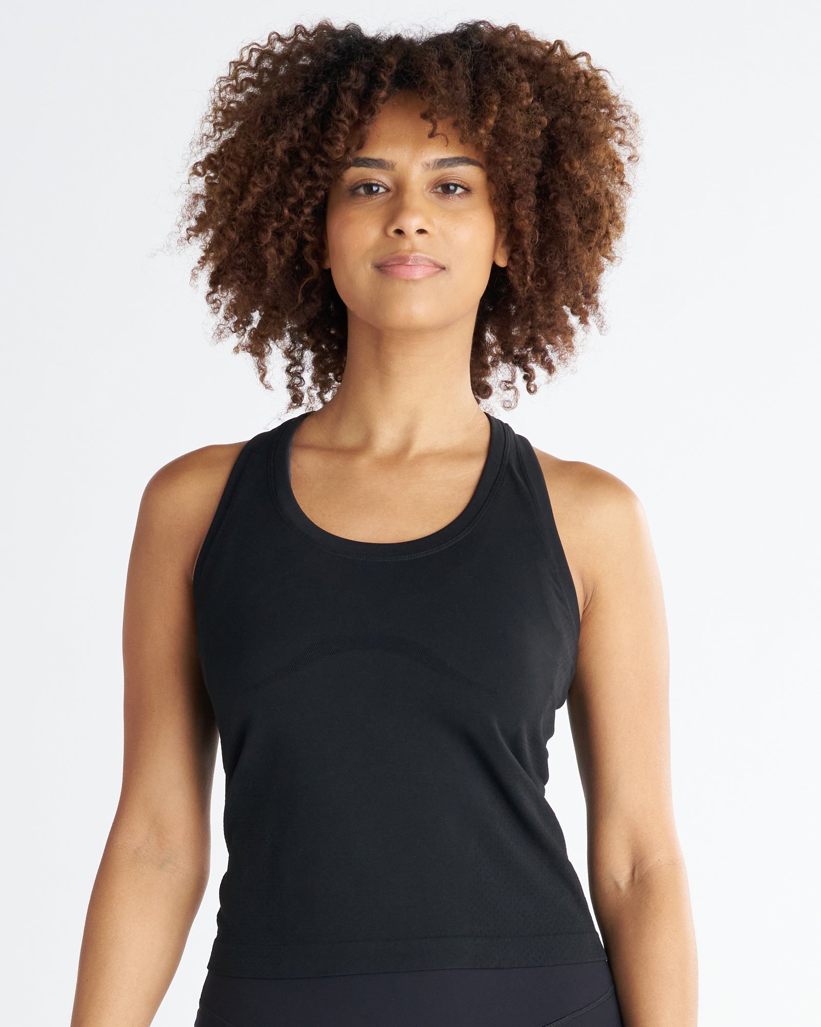 Women's Seamless Tank in black, front view on model with curly hair, featuring a scoop neck and racerback silhouette.
