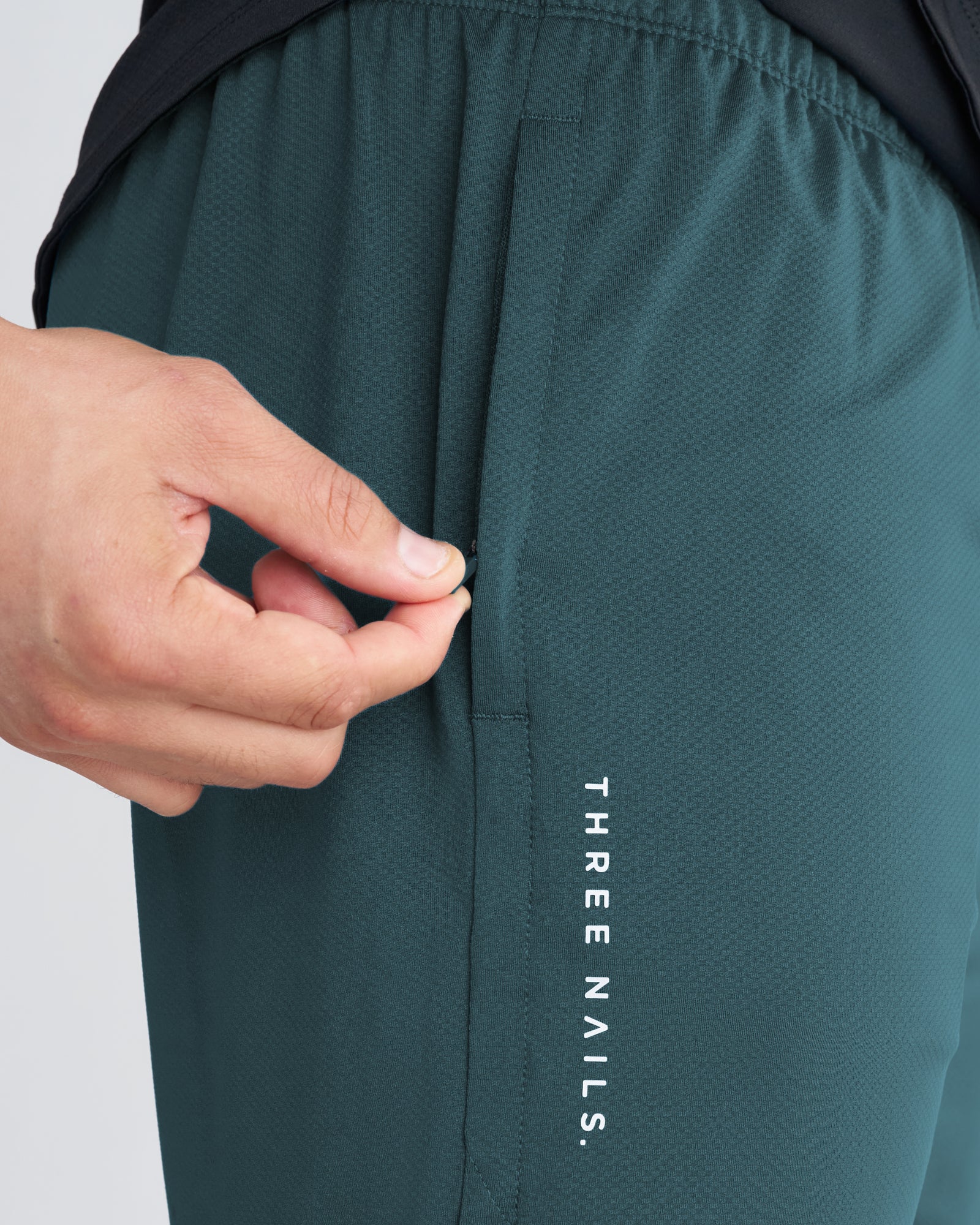 Close-up of Pro-Tech 2.0 Liner Short in teal showing zippered side pocket detail with hand reaching in.