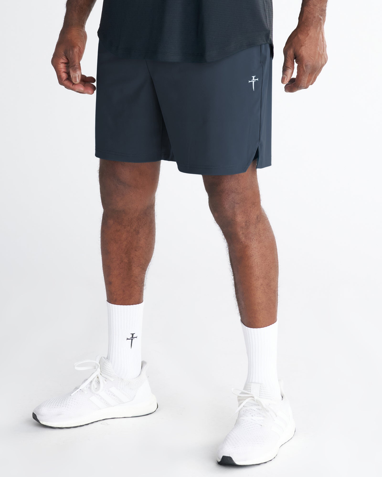 Front angle view of Vapor-Lite Liner Short in Midnight Navy with small cross logo, worn with white socks and sneakers.