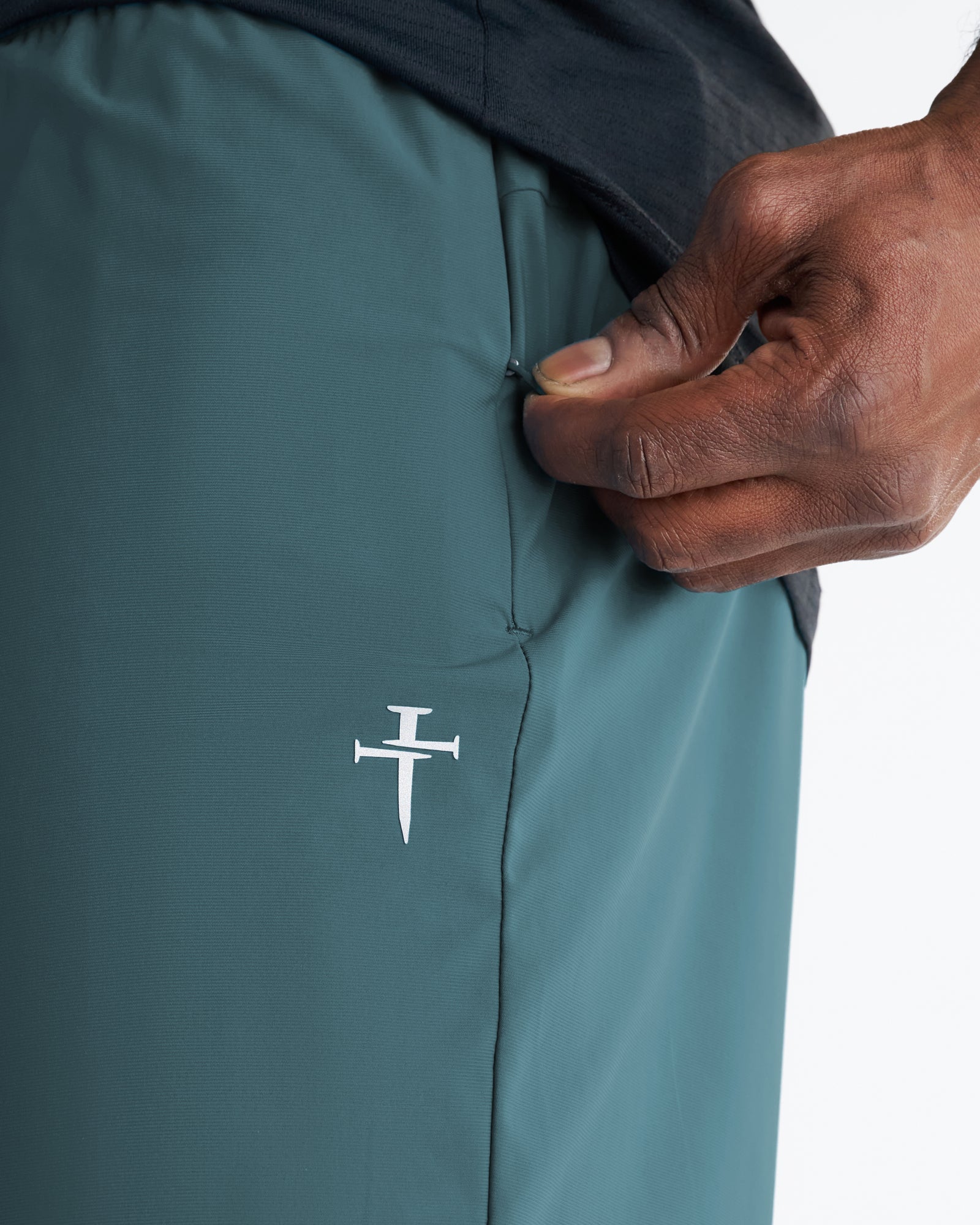 Close-up of Vapor-Lite Liner Short in teal showing side pocket detail and embroidered cross logo.