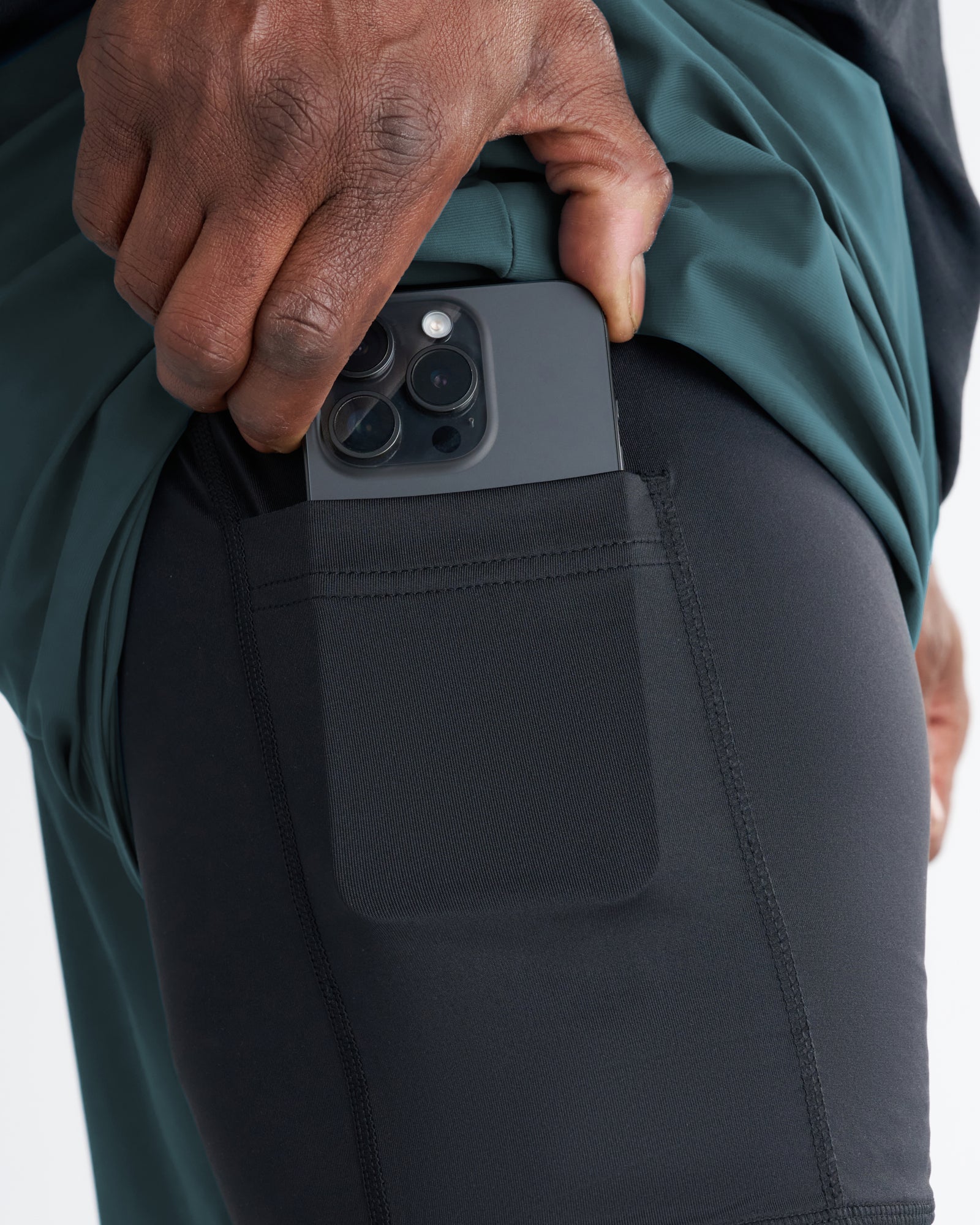 Close-up of Vapor-Lite Liner Short Cross in Teal showing side phone pocket with an iPhone being inserted.