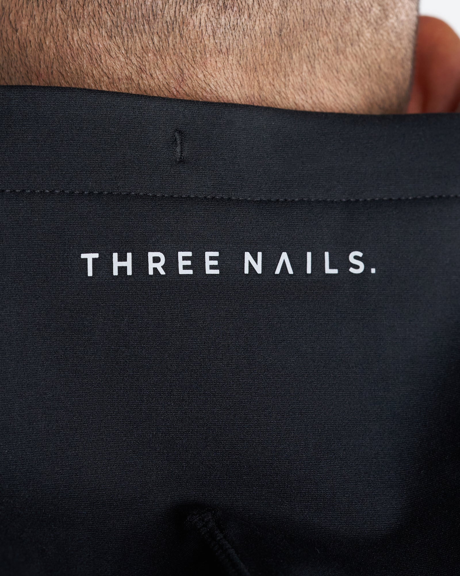 Close-up of the Haven Performance Hoodie in black showing the Three Nails. logo printed on the upper back.