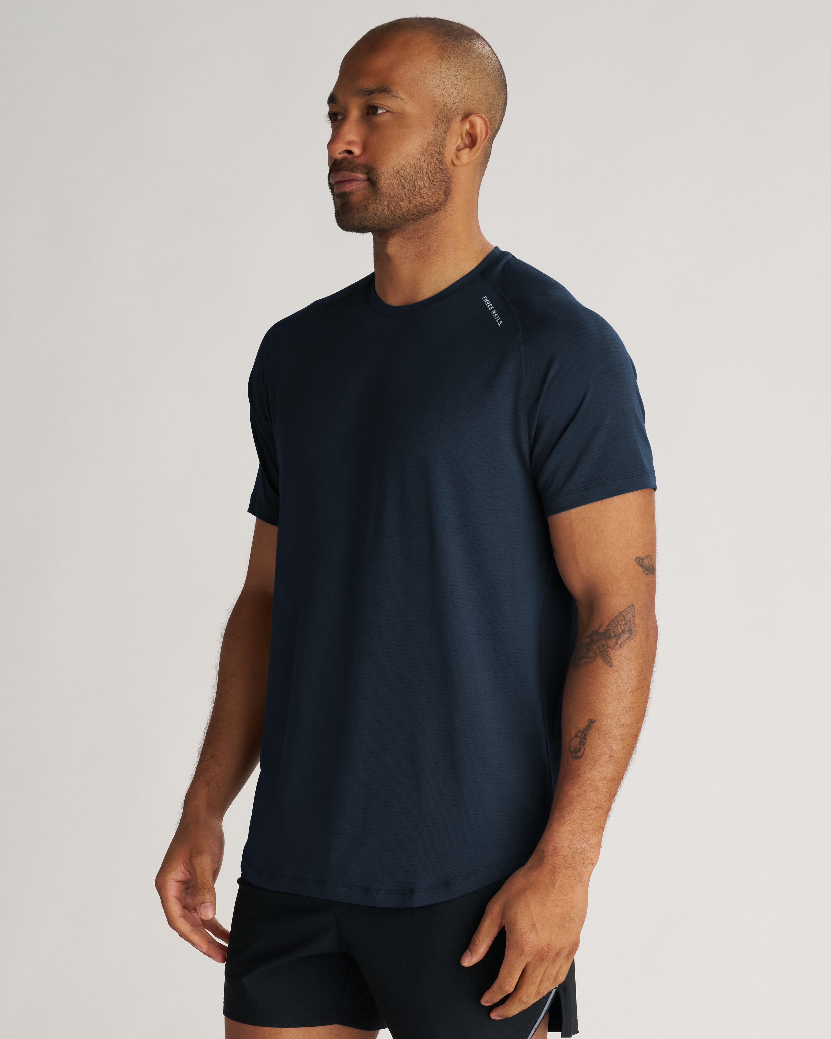 Aion-Lite Tee Midnight Navy on male model, three-quarter front view, fitted navy performance tee with black shorts.