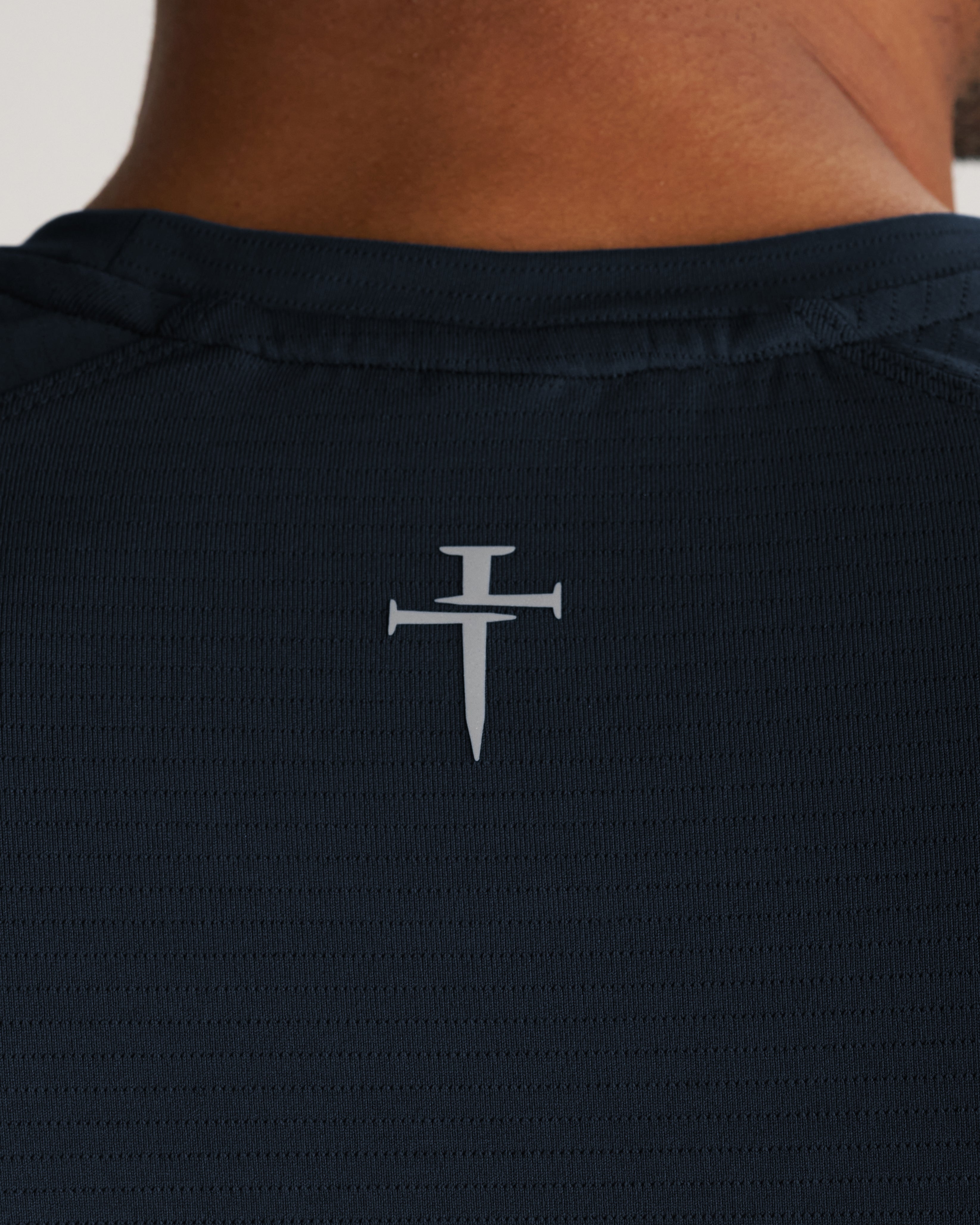 Close-up back neck detail of the Aion-Lite Tee in Midnight Navy showing the Three Nails cross logo.