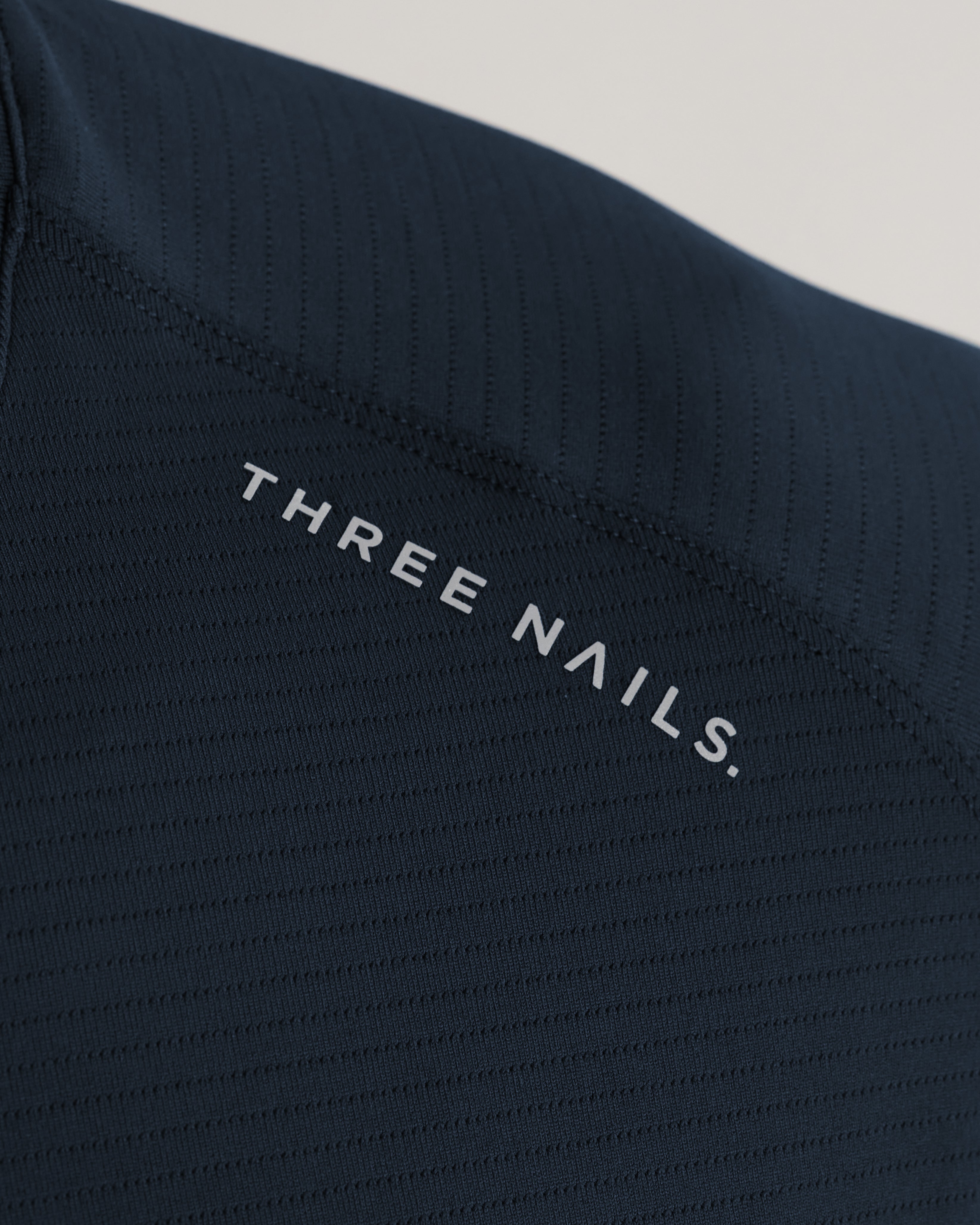 Close-up detail shot of the Aion-Lite Tee Midnight Navy showing the Three Nails chest logo and textured ribbed fabric.