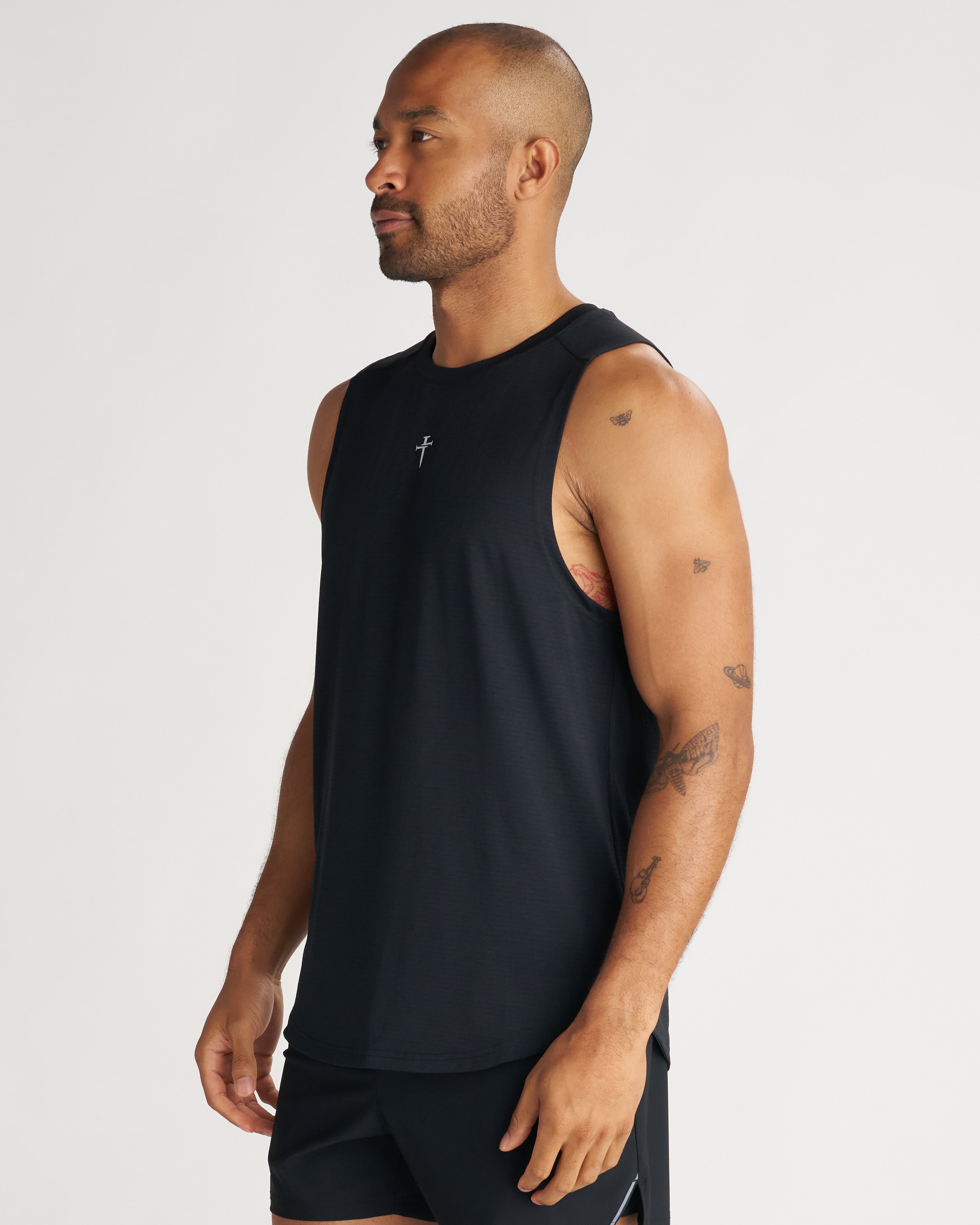 Aion-Lite Tank in black on a male model at a side angle, showing relaxed fit and small cross logo at chest.