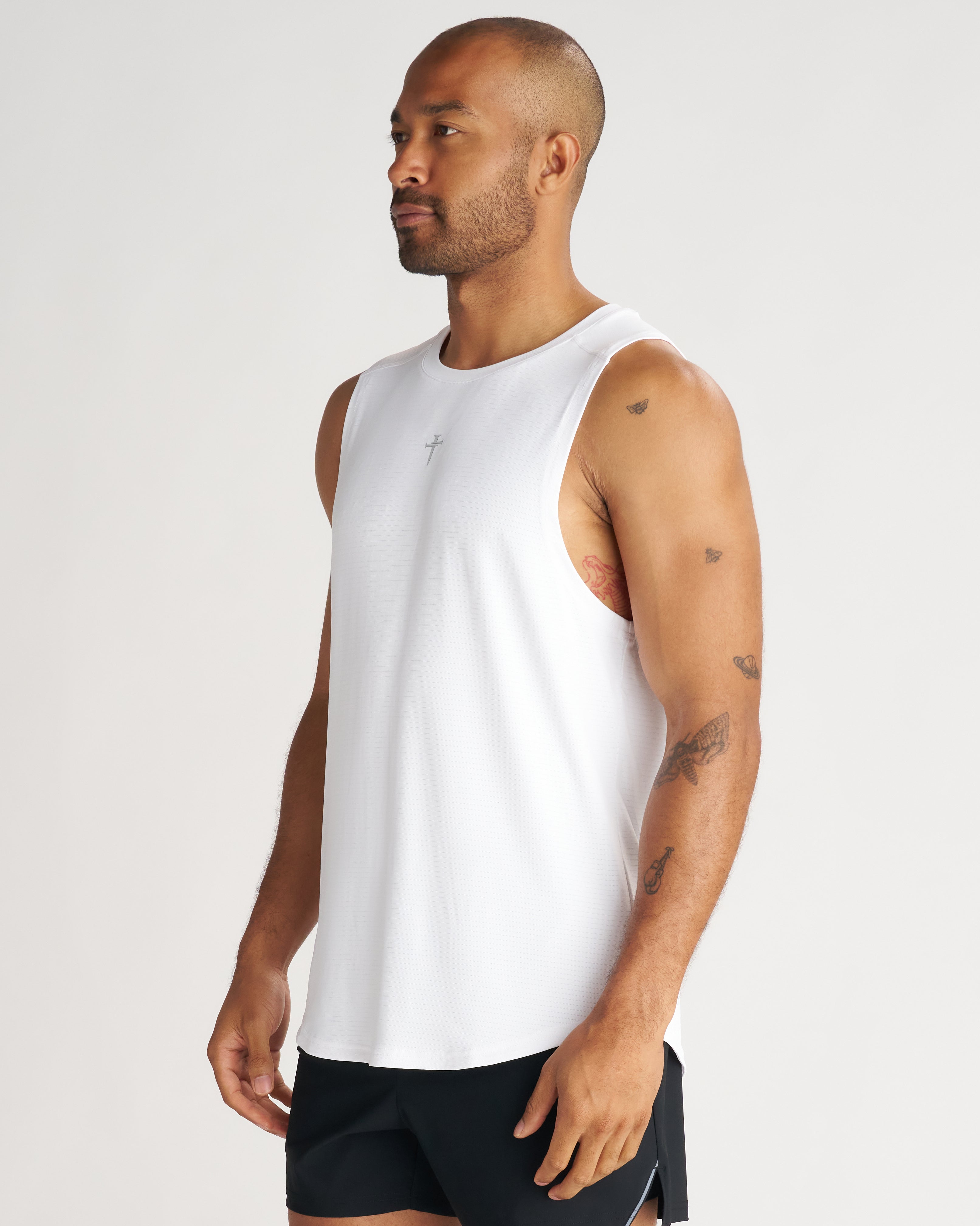 Man wearing white Aion-Lite Tank at a side angle, showing relaxed fit, cut-off sleeves, and small cross logo.
