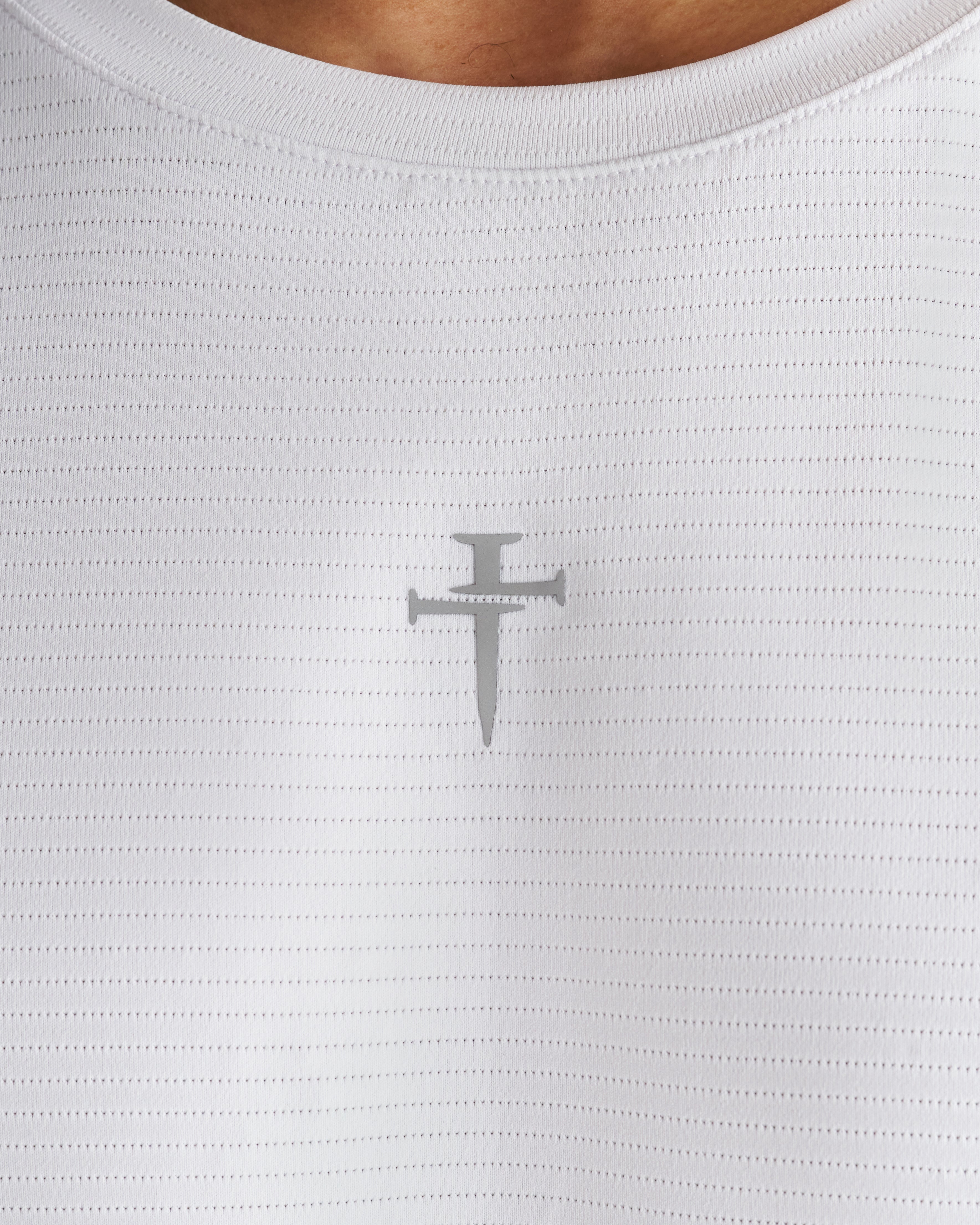 Close-up of the white Aion-Lite Tank chest area showing the subtle gray Three Nails cross logo on textured mesh fabric.
