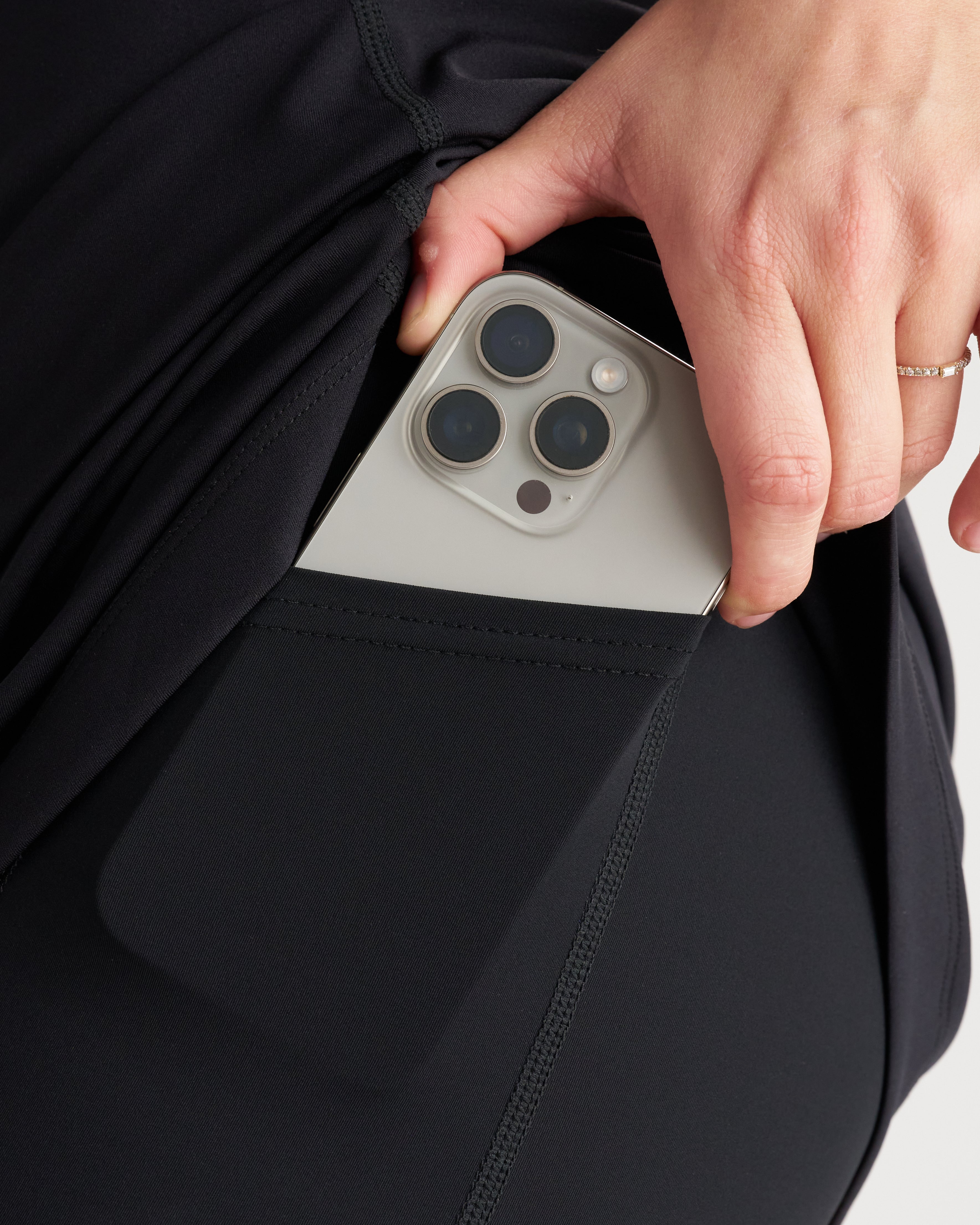 Close-up of the Links Golf Dress Black side pocket with a hand inserting a silver iPhone Pro.